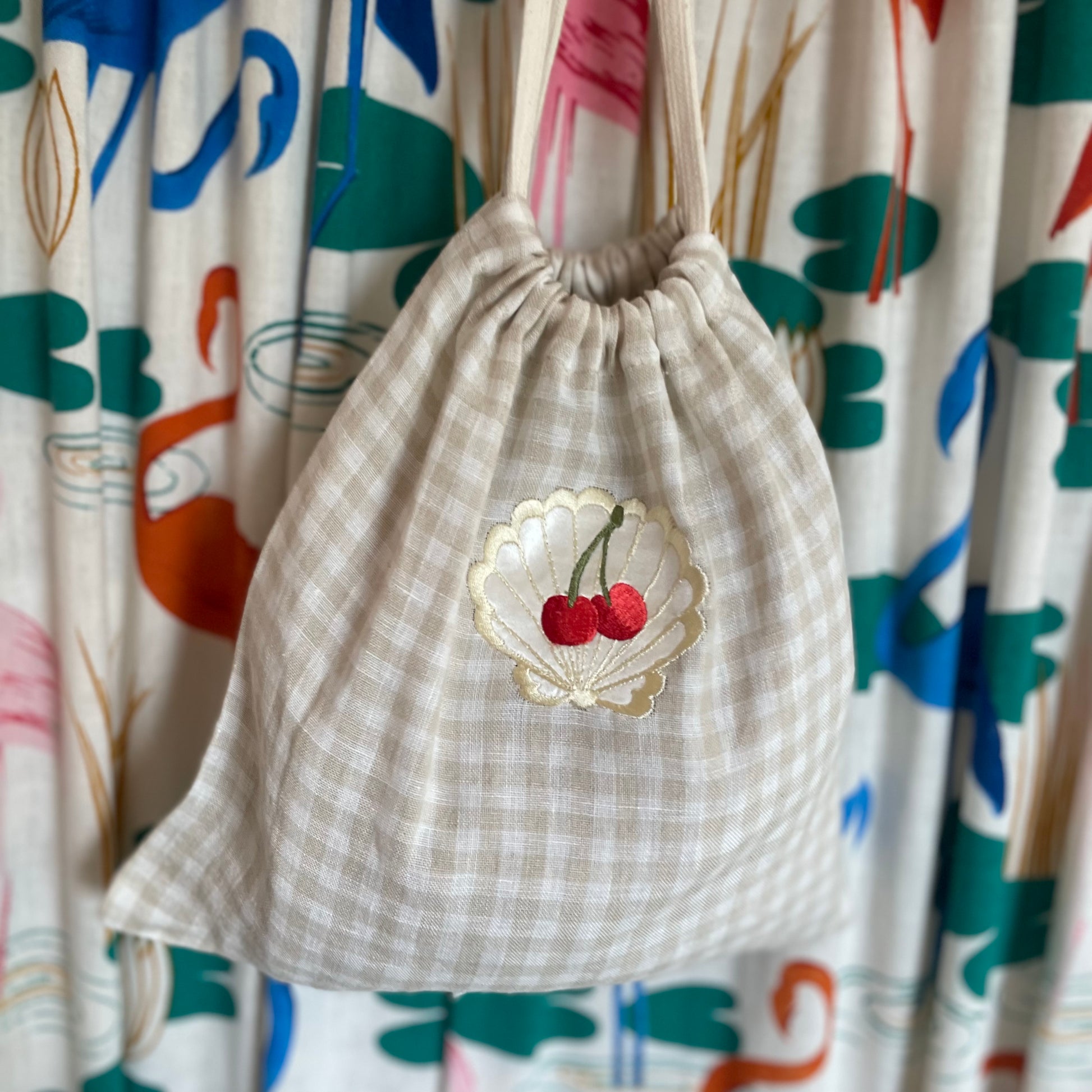 Linen drawstring bag with embroidered cherries hanging against a patterned cloth