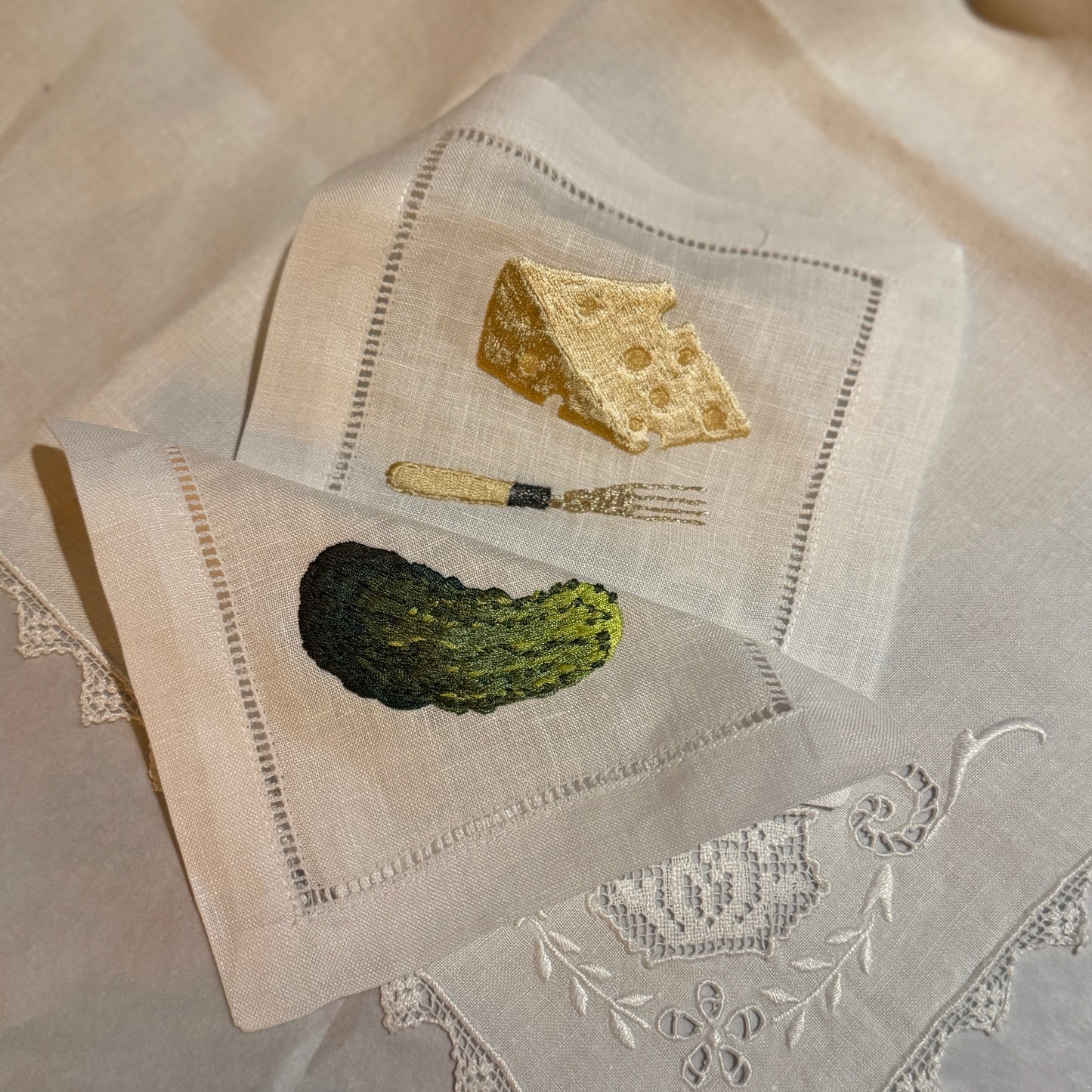 Embroidered napkins with cheese and pickle design on a textured fabric background