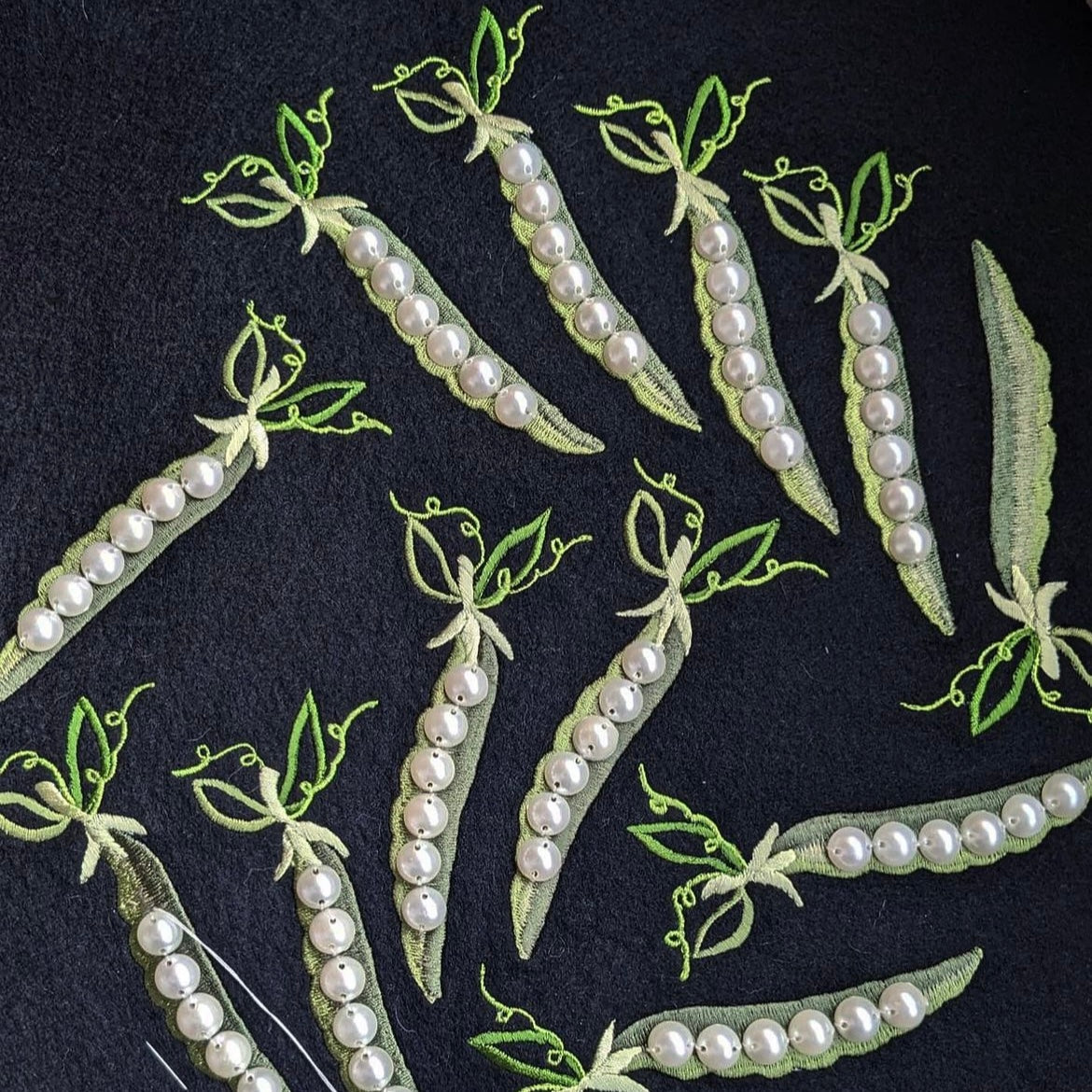 Embroidered pea and pearl patches on black felt before they are finished and cut out