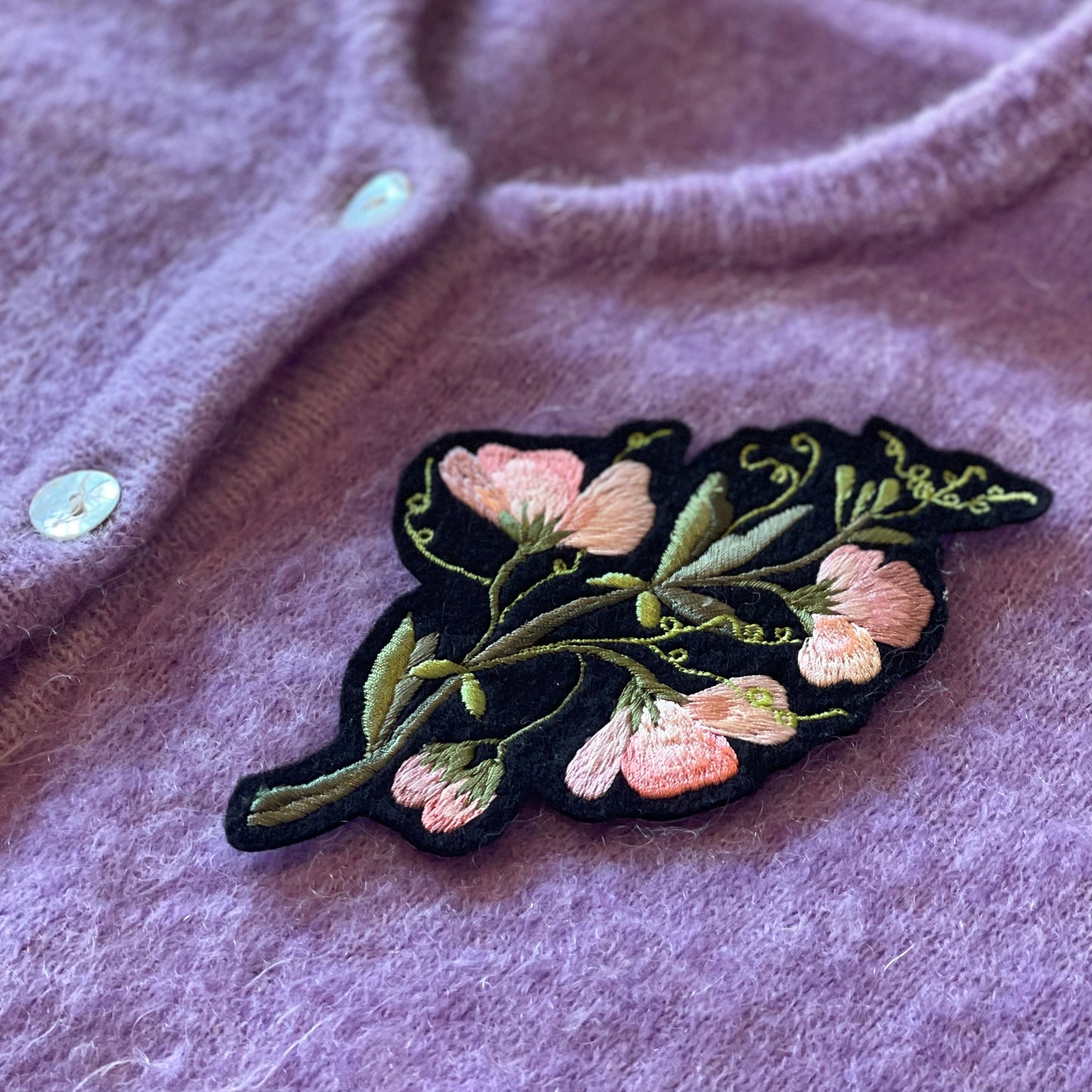 Sweet pea embroidered patch shown on the front chest of a lilac cardigan