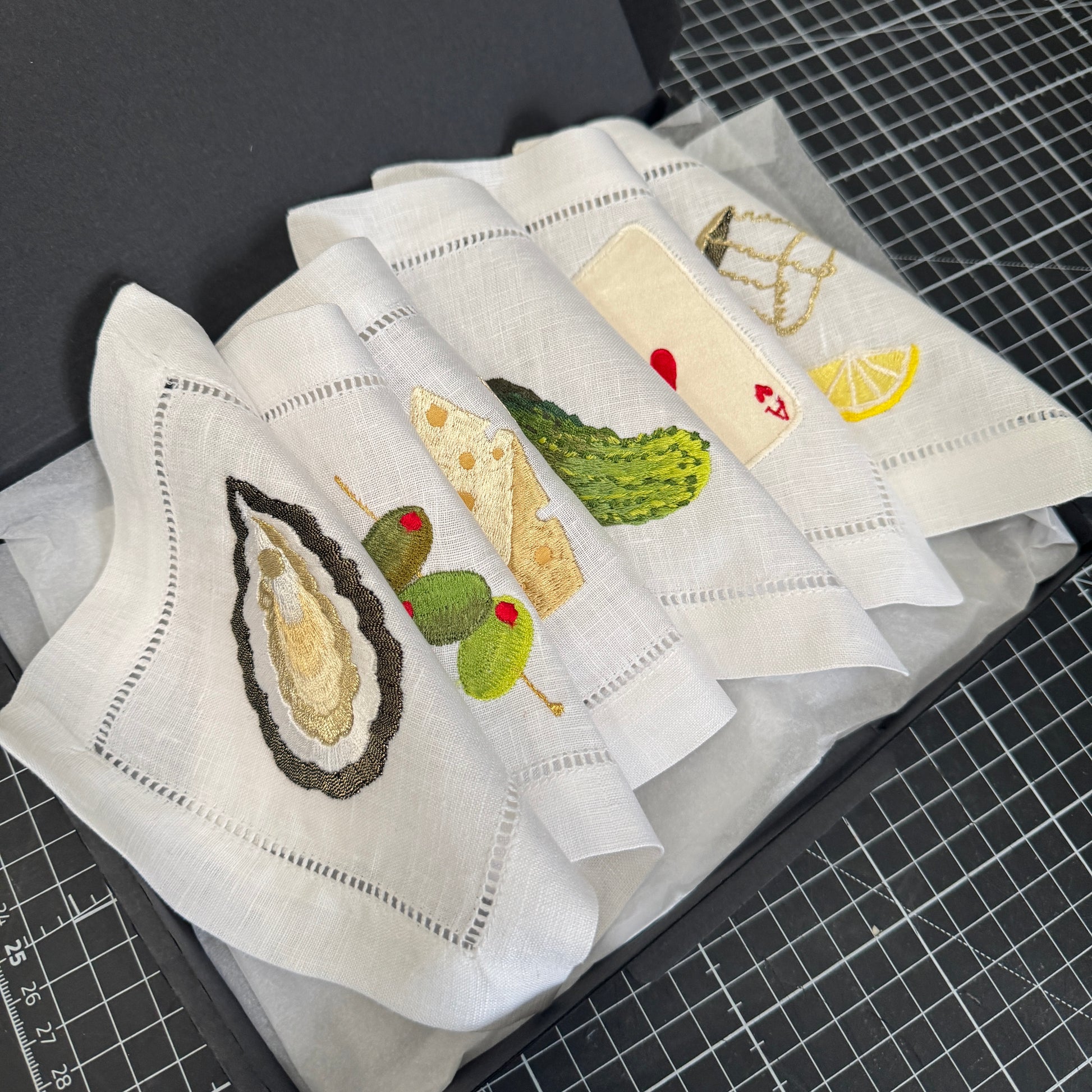 Set of embroidered napkins with cocktail party illustrations on a cutting mat.