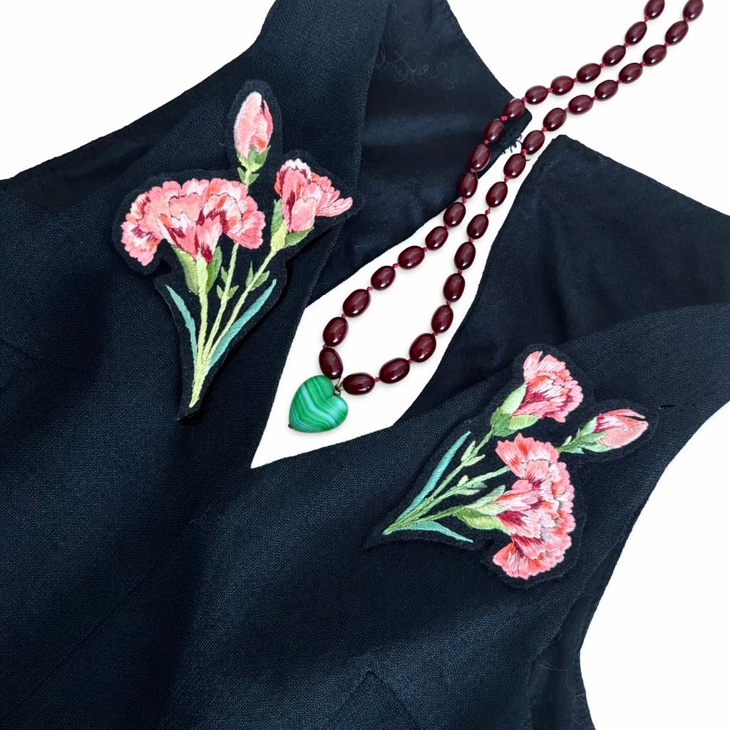 Black fabric with pink floral embroidery and a necklace on a white background