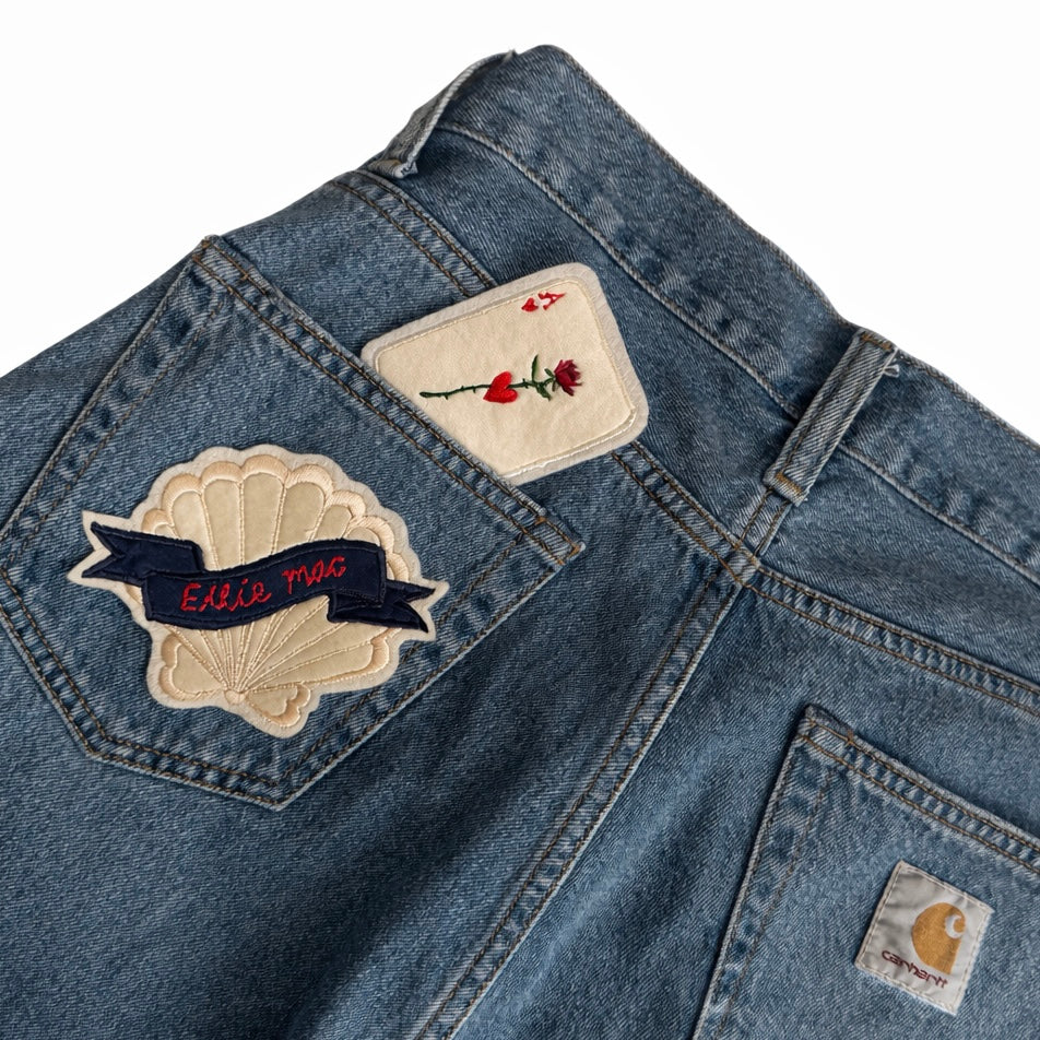 Close-up of a denim shorts with patches and a visible brand logo on a white background