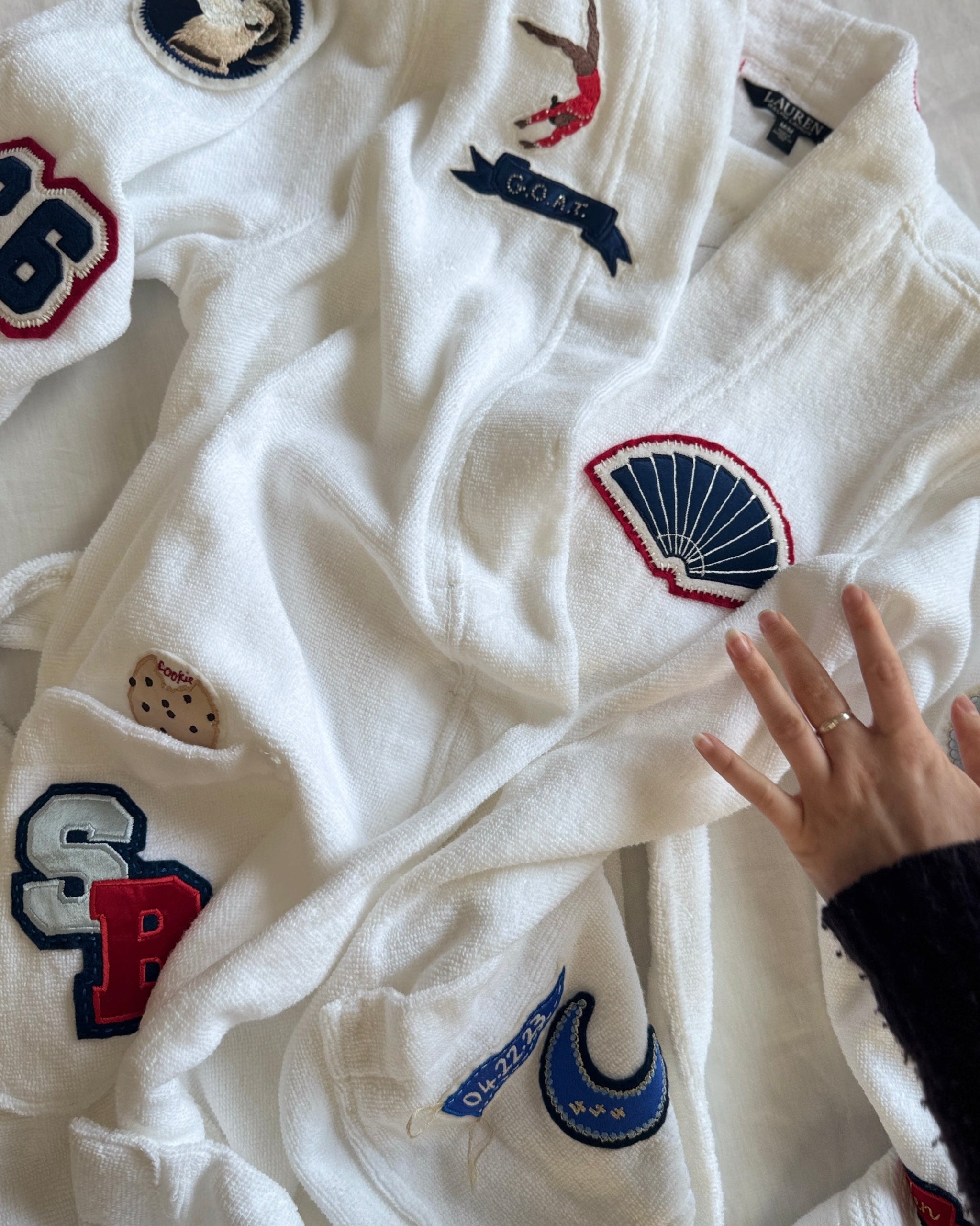 White robe with embroidered logos and a hand touching it