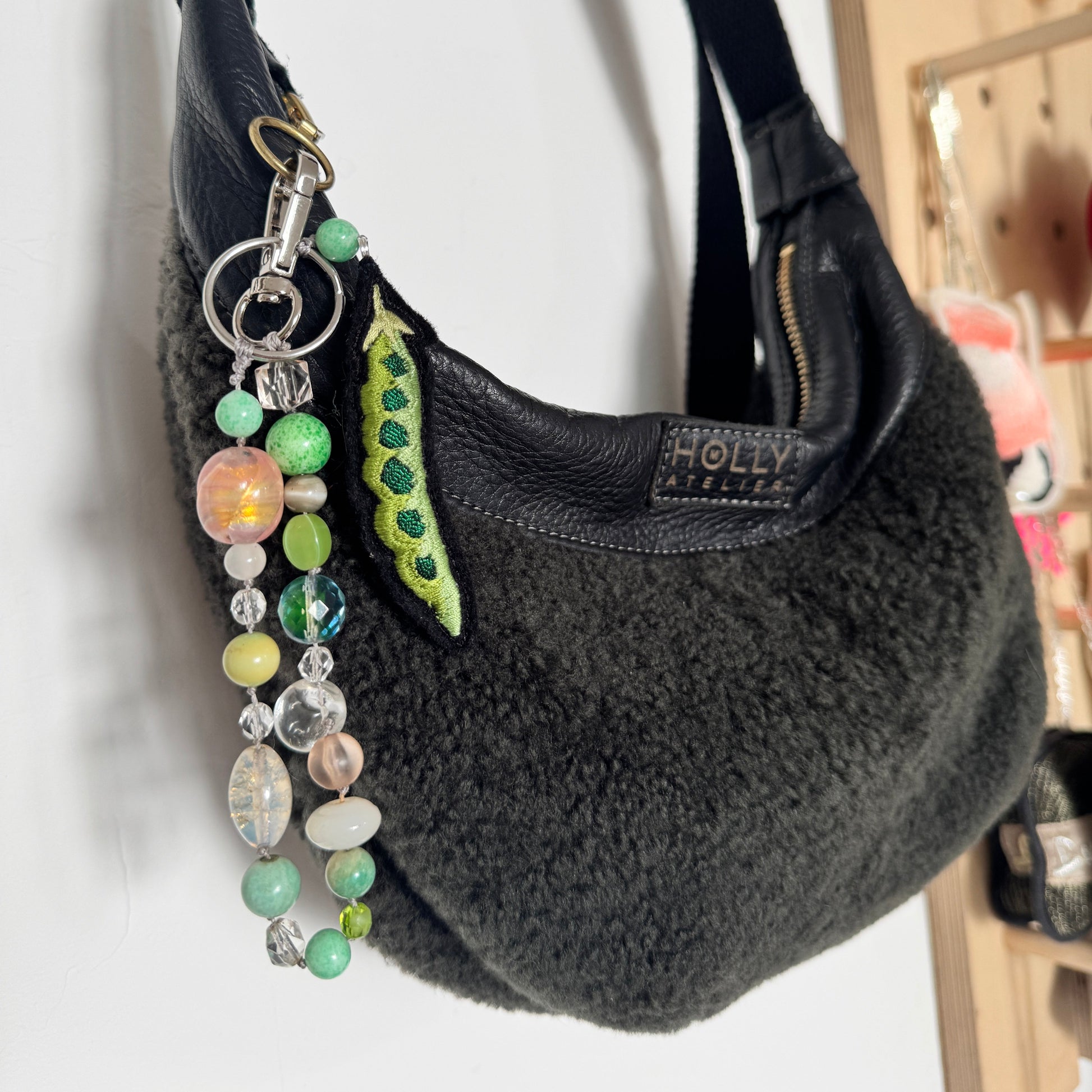 Black textured handbag with a colorful beaded keychain and 'Holly M Atelier' brand bag.