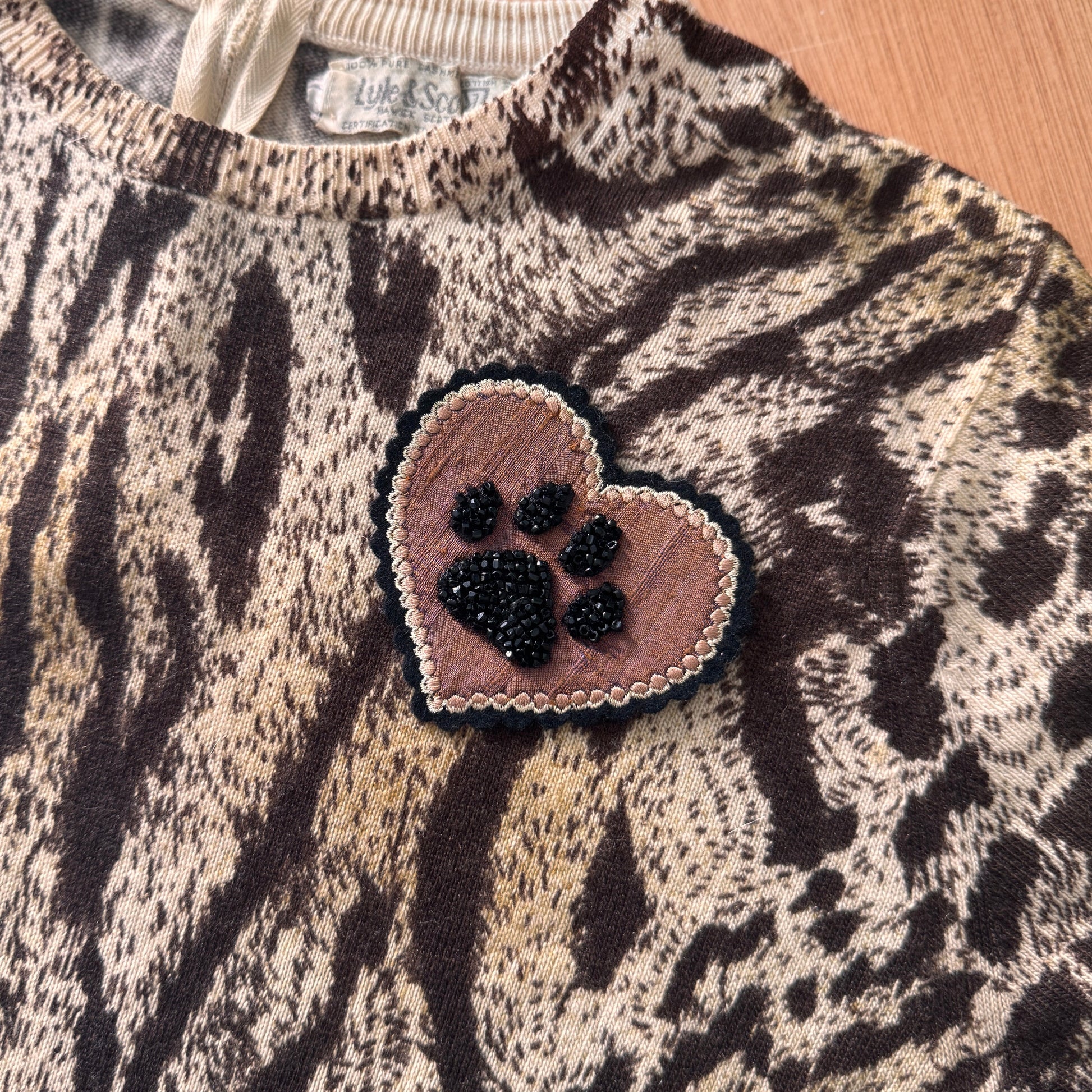 Leopard print sweater with a heart-shaped paw print patch on a wooden surface