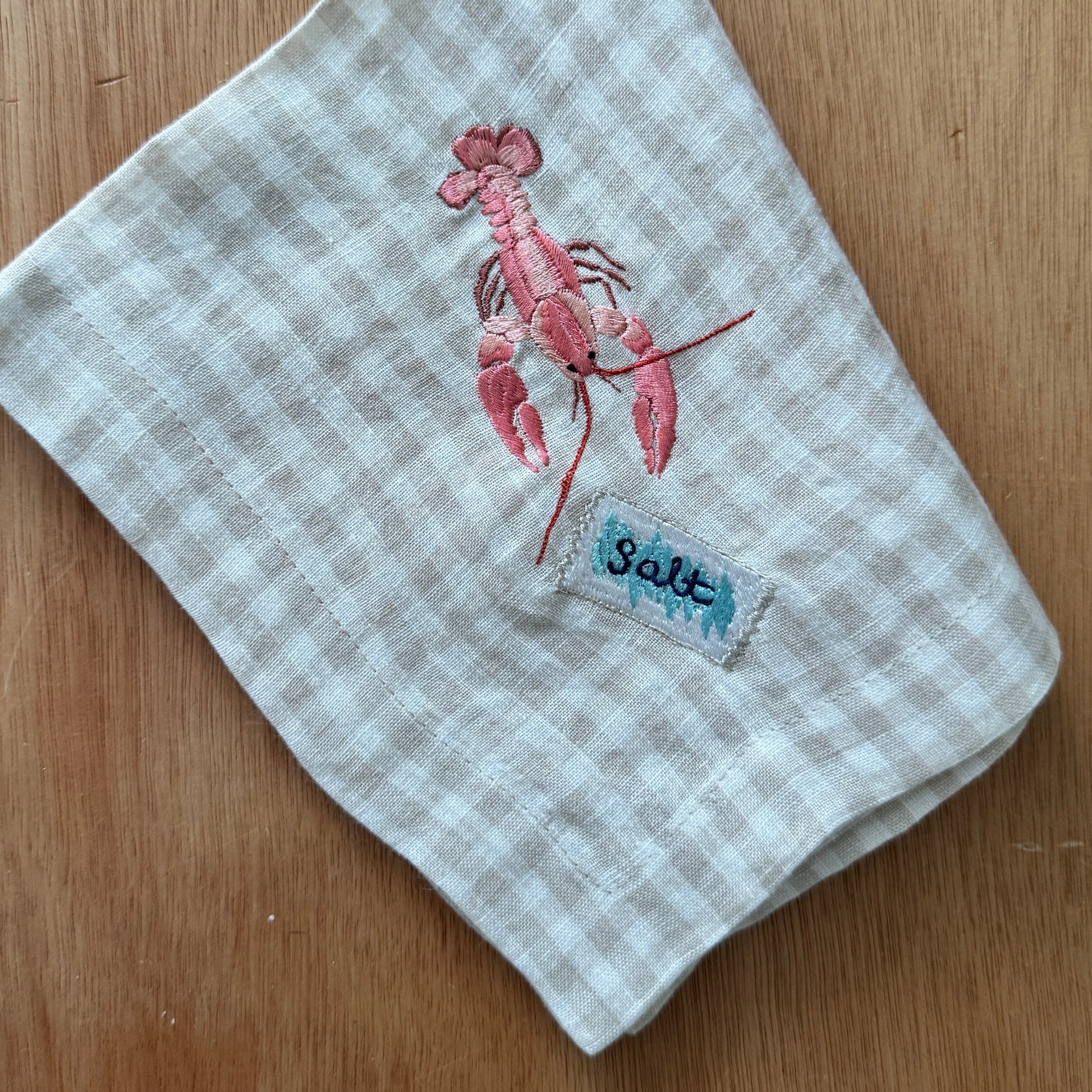 Embroidered towel with a crayfish design and 'Salt' label on a wooden surface