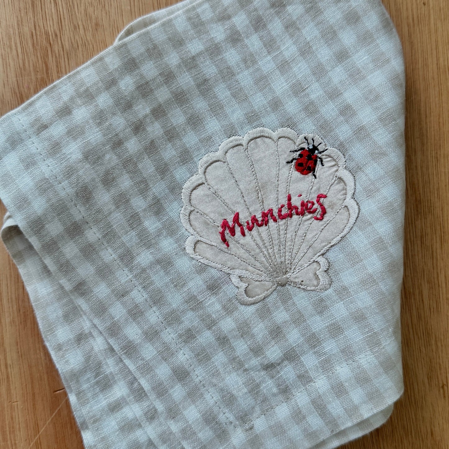 Gray checkered napkin with a shell design and 'Munchies' text on a wooden surface