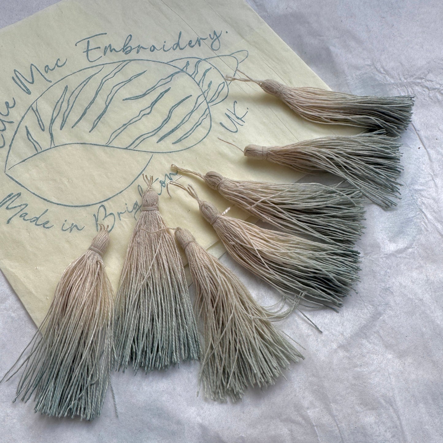 Set of tassels on a piece of paper with embroidery design and text.