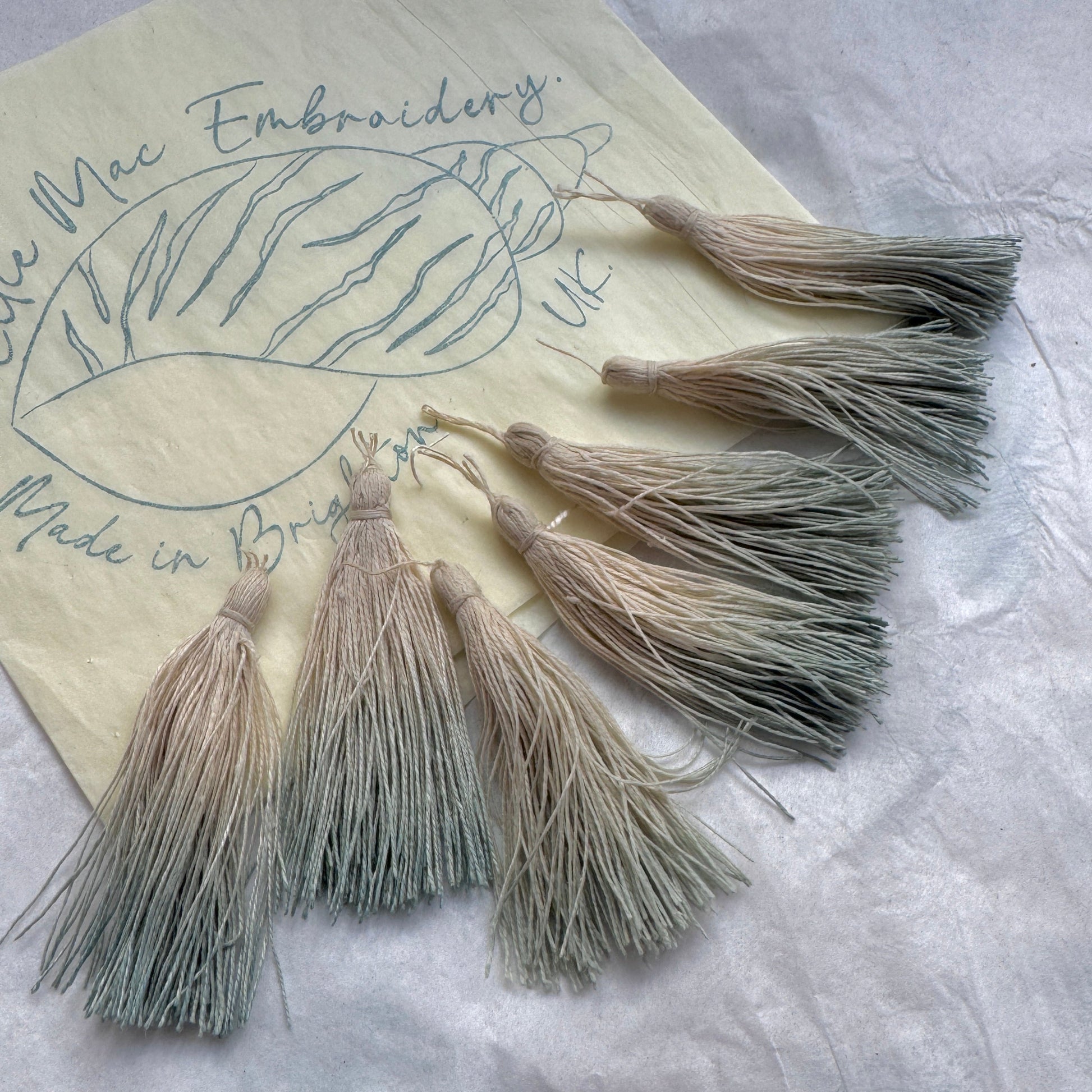 Set of tassels on a piece of paper with embroidery design and text.
