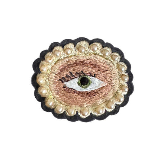 Embroidered patch with an eye design surrounded by pearls on a white background