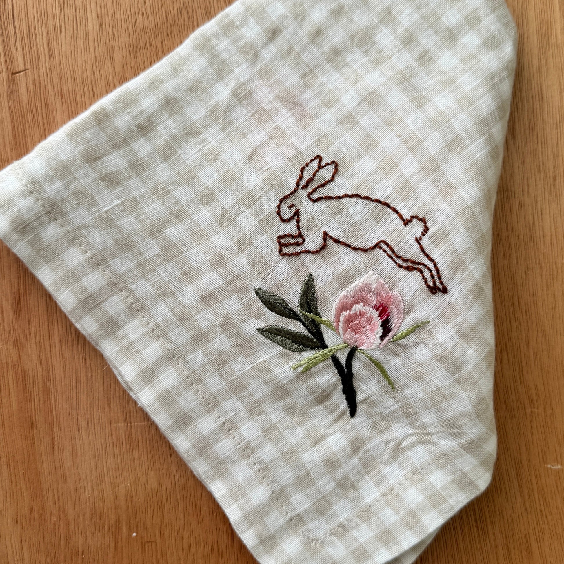Embroidered fabric with a rabbit and flower design on a wooden surface