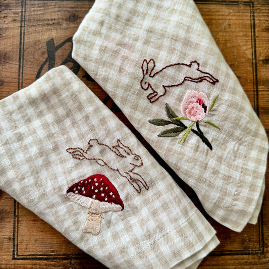 Two embroidered towels with rabbit and mushroom designs on a wooden surface