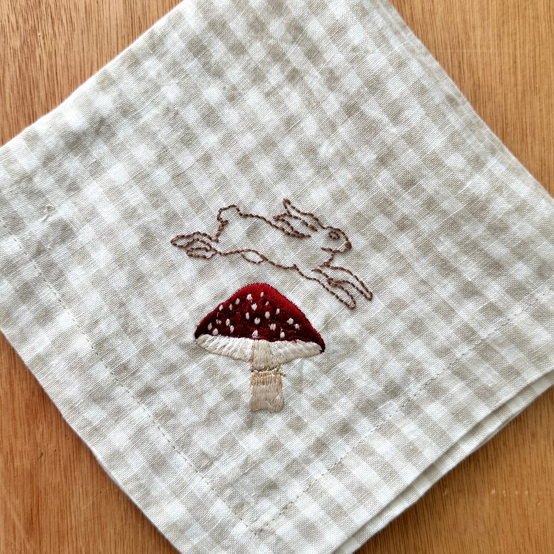 Embroidered napkin with a rabbit and mushroom design on a checkered background