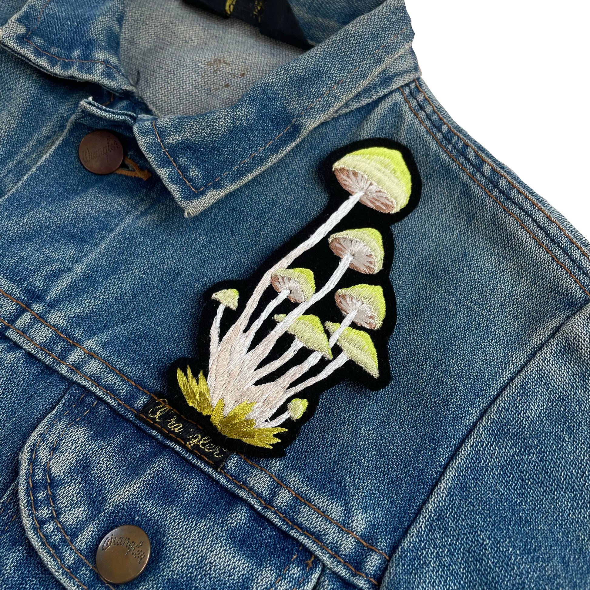 Green cluster mushrooms embroidered patch shown on the top front shoulder of a denim jacket