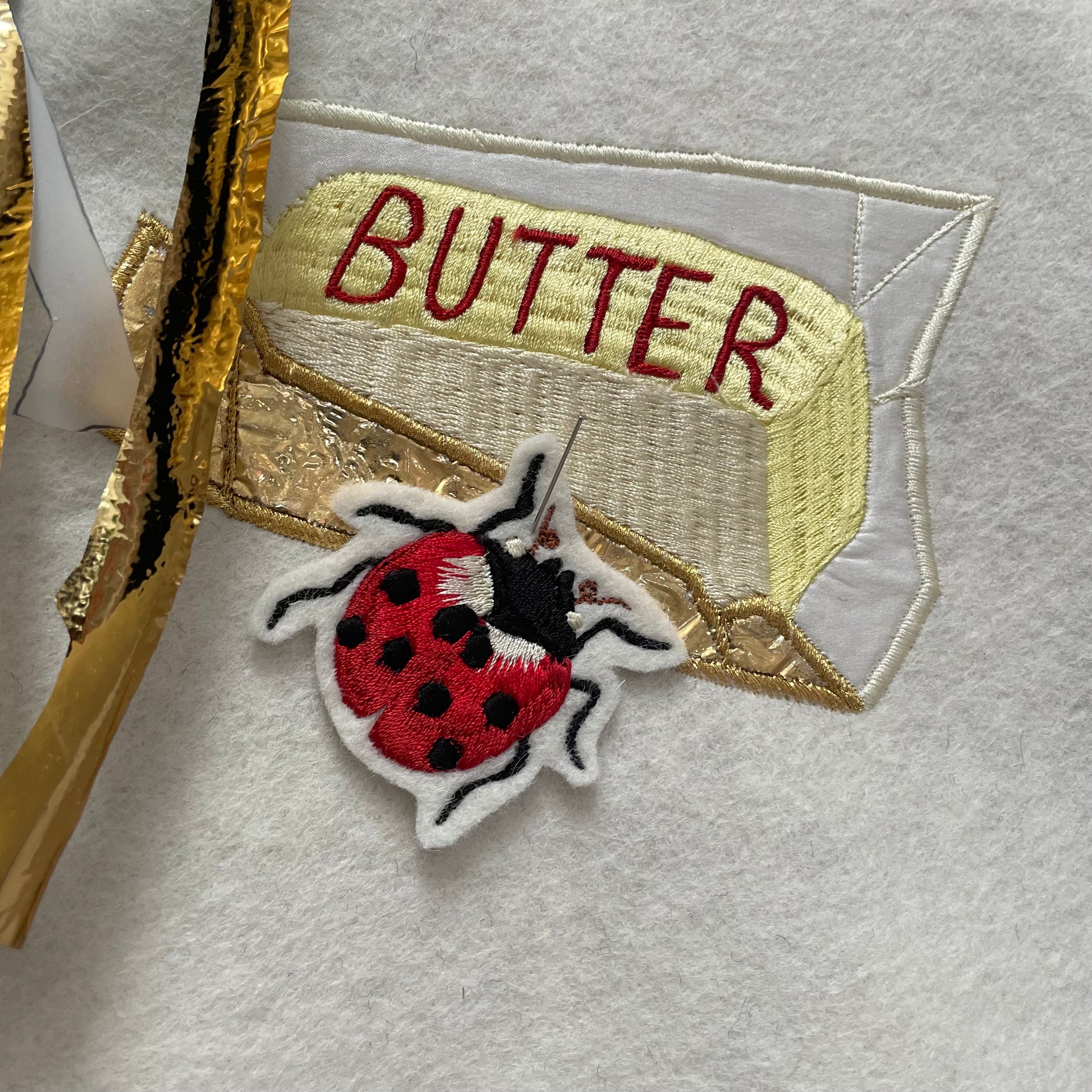 Small ladybird embroidered patch shown pinned to some embroidered artwork of butter
