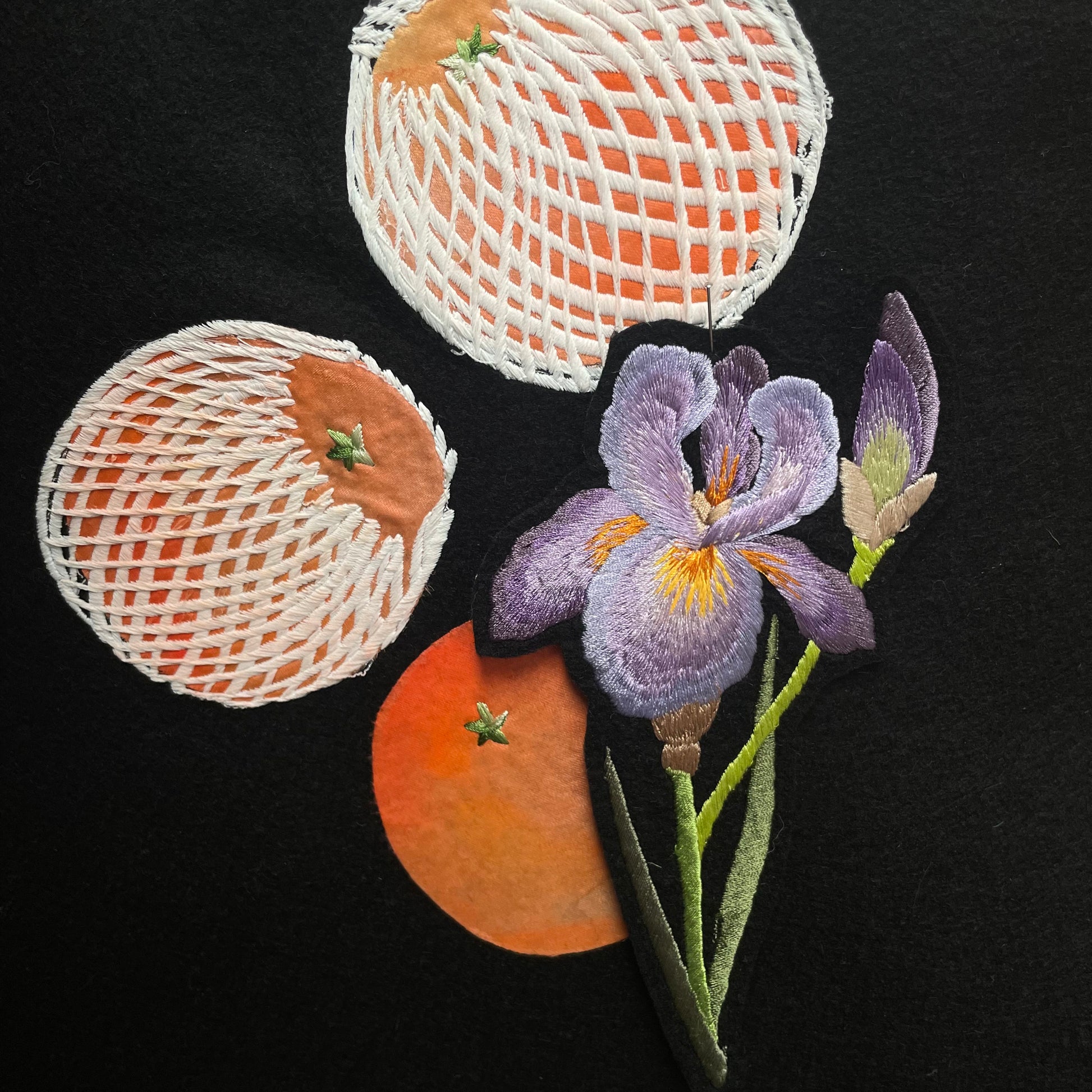 Iris embroidered patch pinned to black felt that has embroidered oranges on
