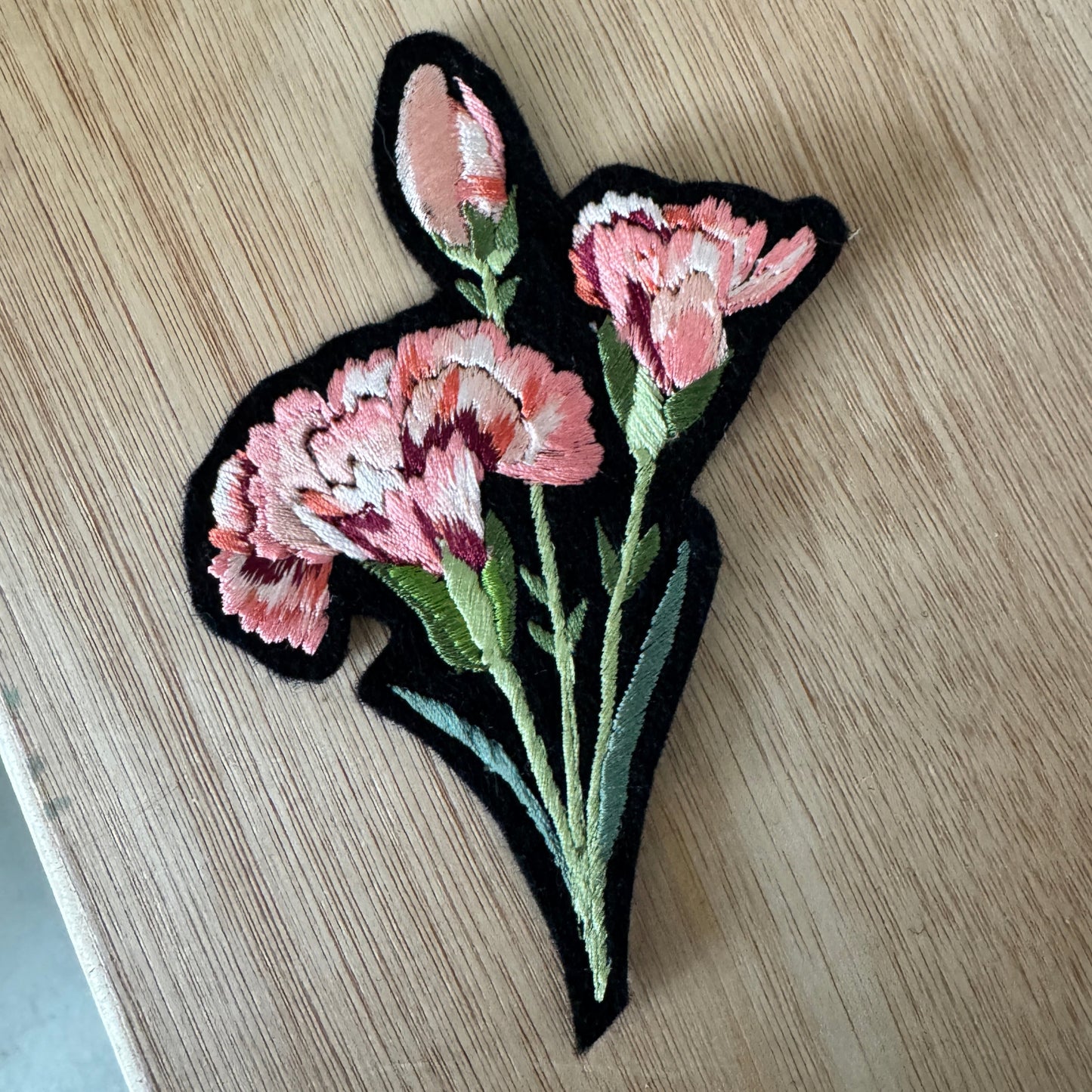 Embroidered patch with pink flowers on a wooden surface