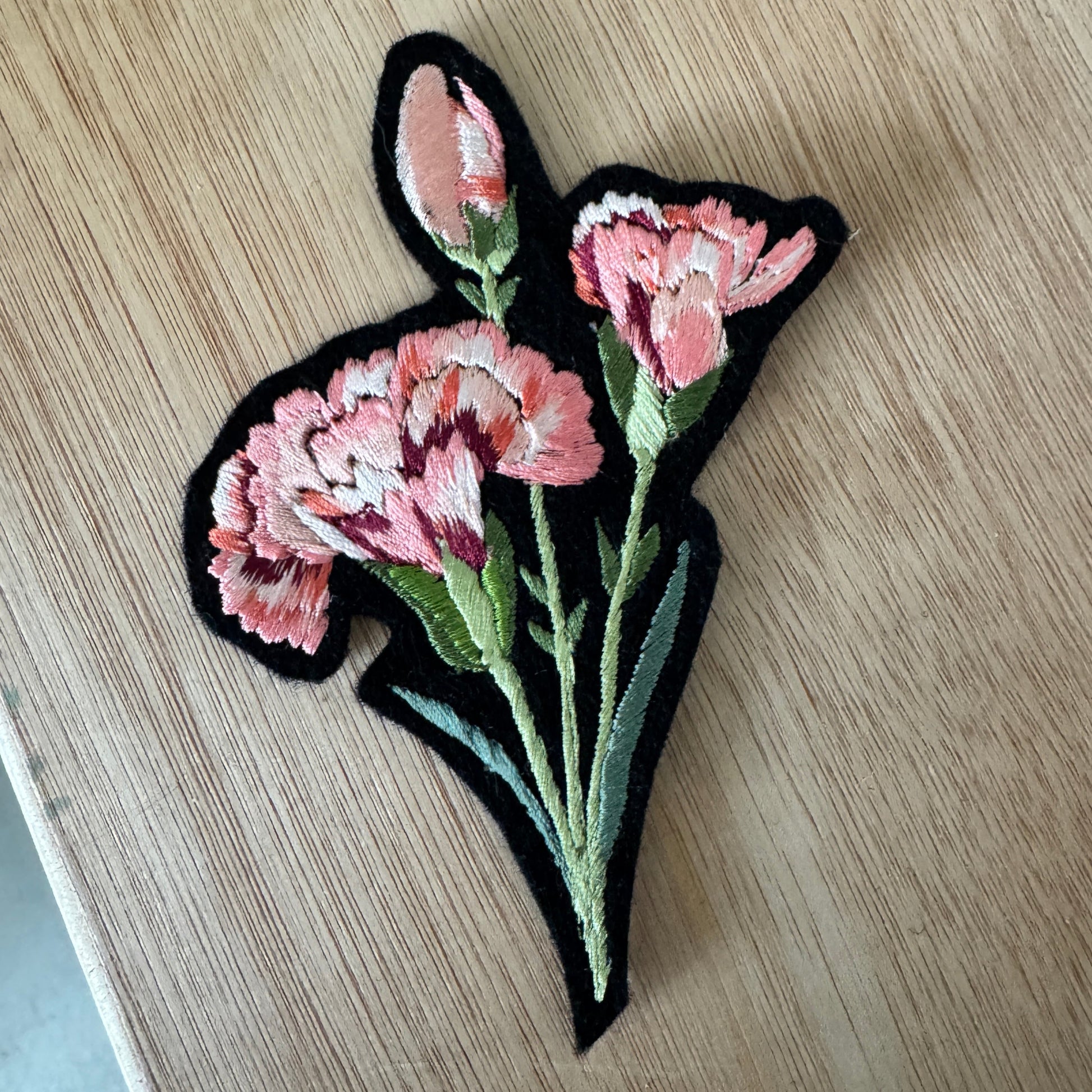 Embroidered patch with pink flowers on a wooden surface