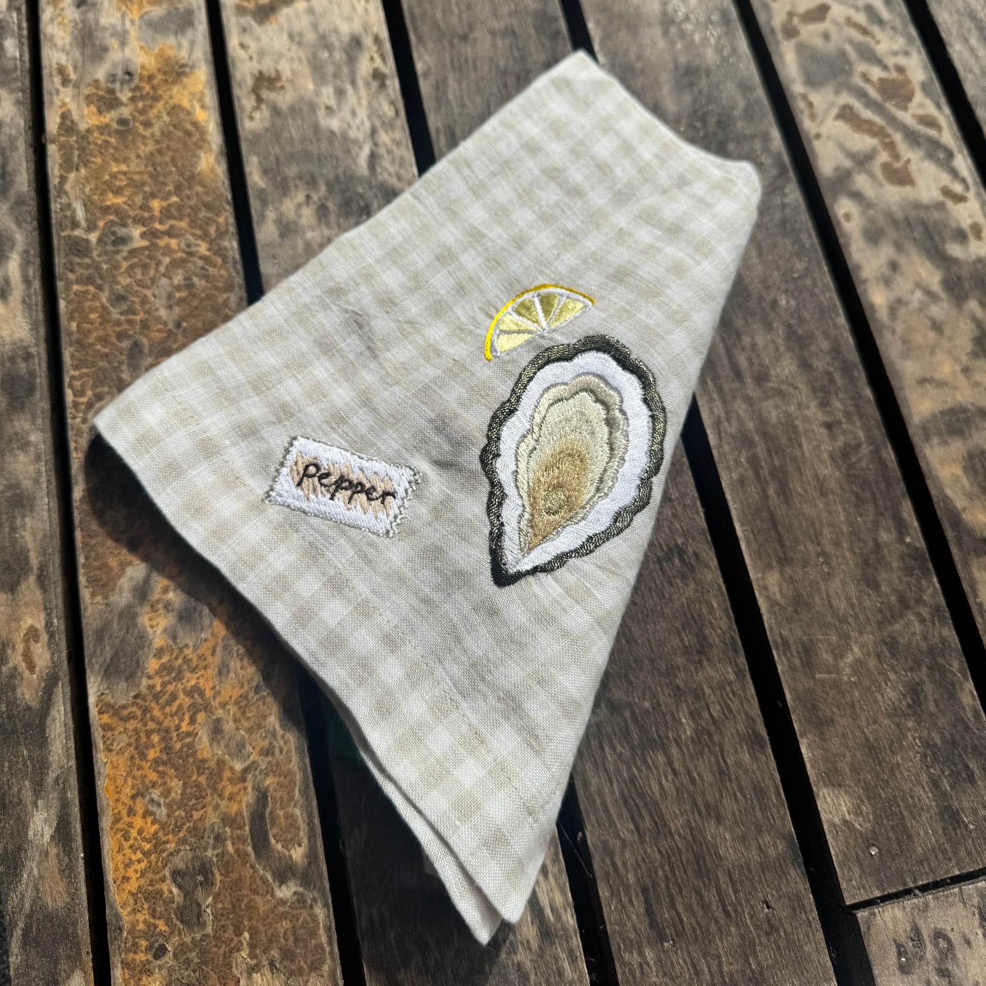 Embroidered napkin with oyster design and 'pepper' on wooden surface