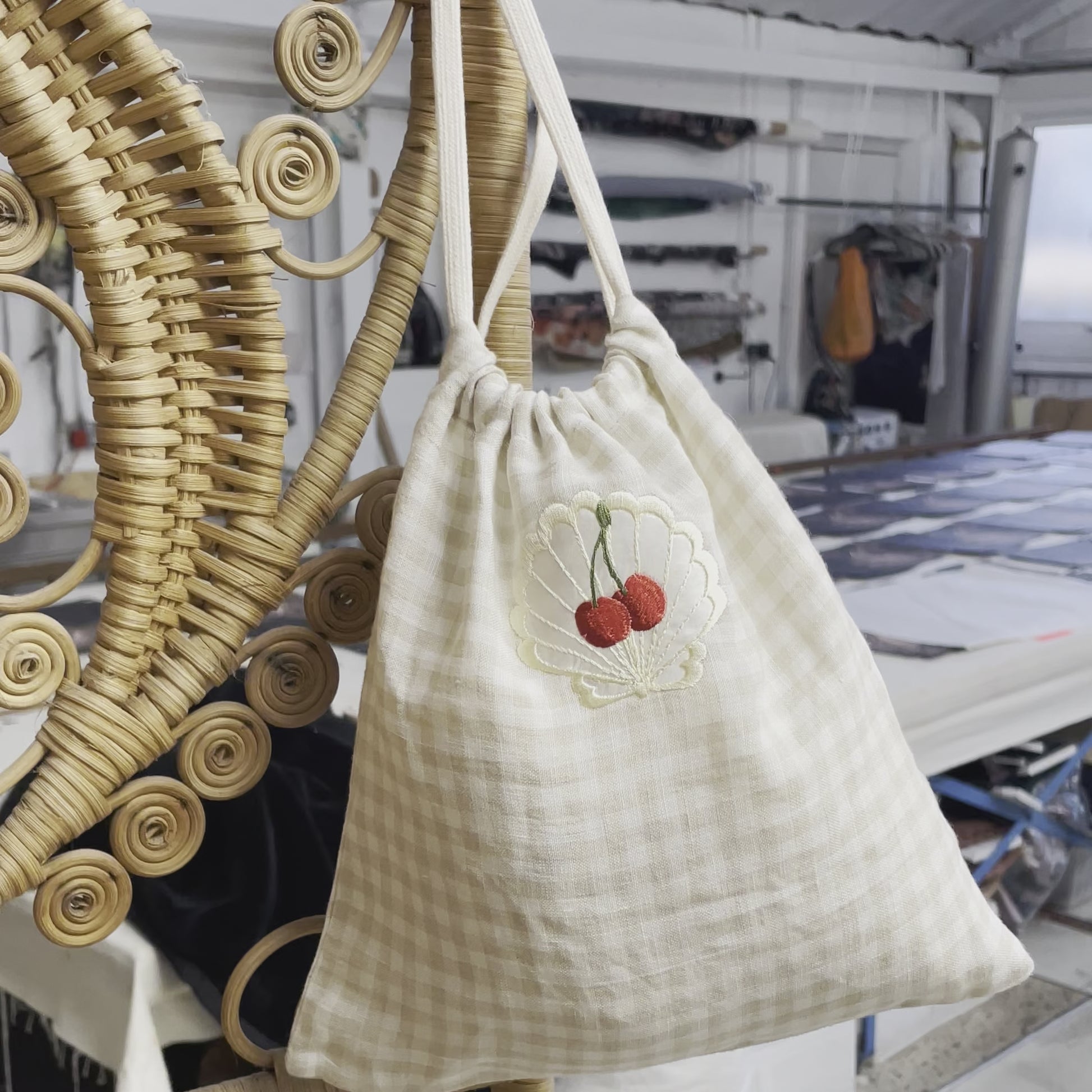 Video shows the linen bag with the camera zooming in on the cherry embroidery and a hand titling the bag for the camera. The bag is hanging on the corner of a rattan screen