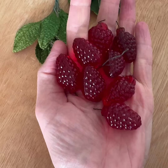 Vintage glass raspberry charms on table. One raspberry has a velvet leaf and wire attached.