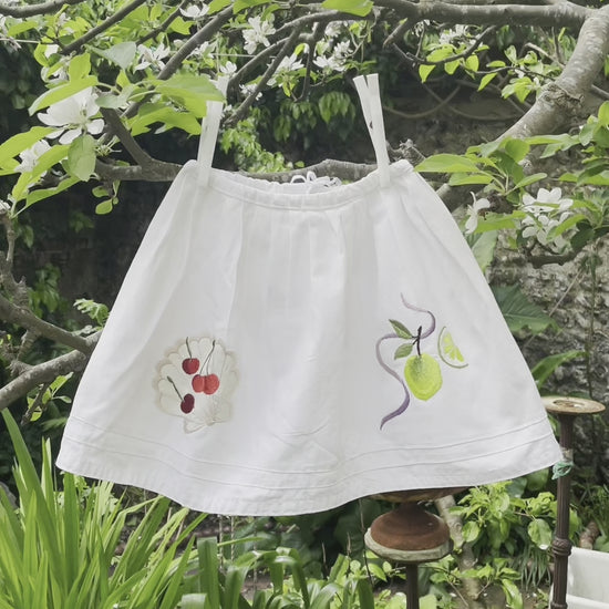 Video reel showcasing Ellie Mac Embroidery's vintage children's clothing collection with close-up of embroidered details. Garments seen hanging from a tree in a garden