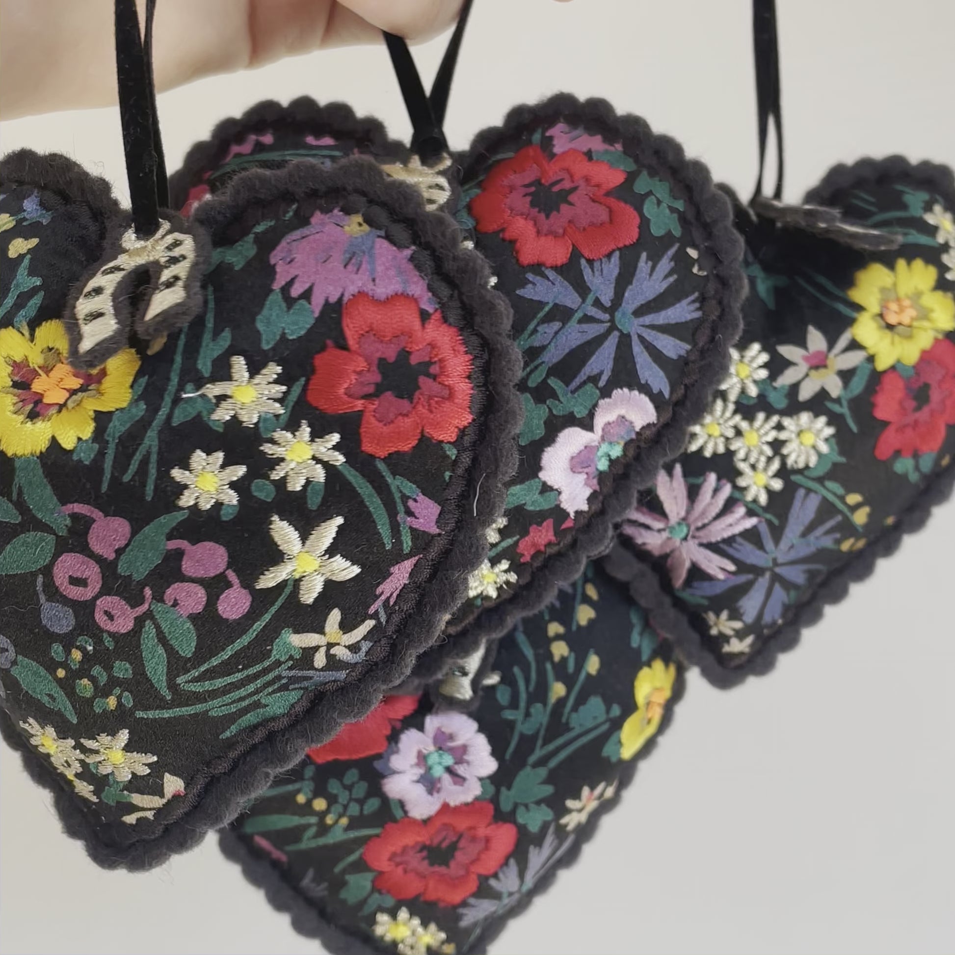 Vidoe of four embroidered padded silk hearts hanging from someone's hand