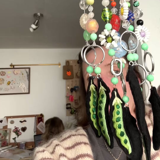 Ellie Mac holding up beaded pea charms in large cluster, held up in front of her face