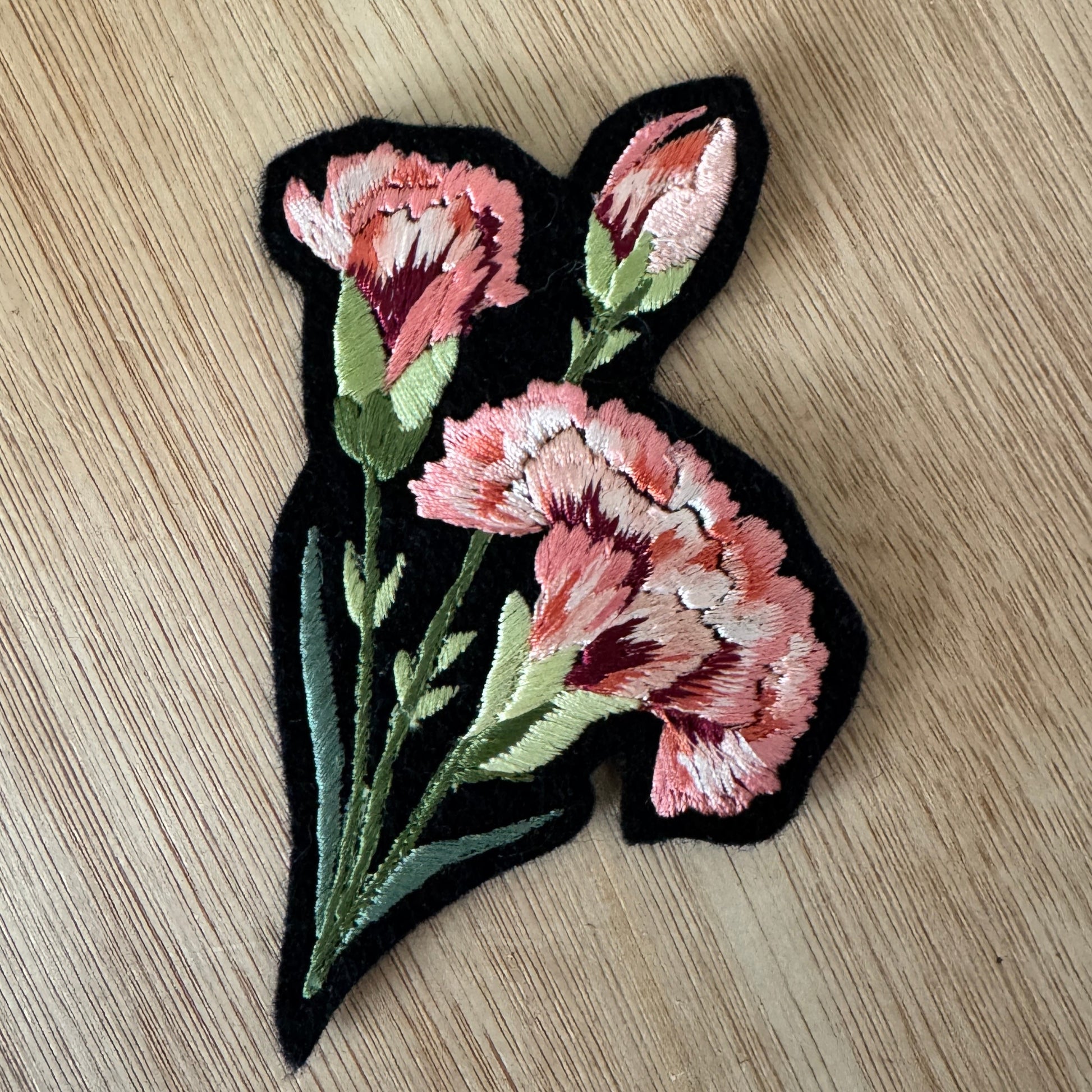 Floral patch with pink flowers on a black background, placed on a wooden surface.