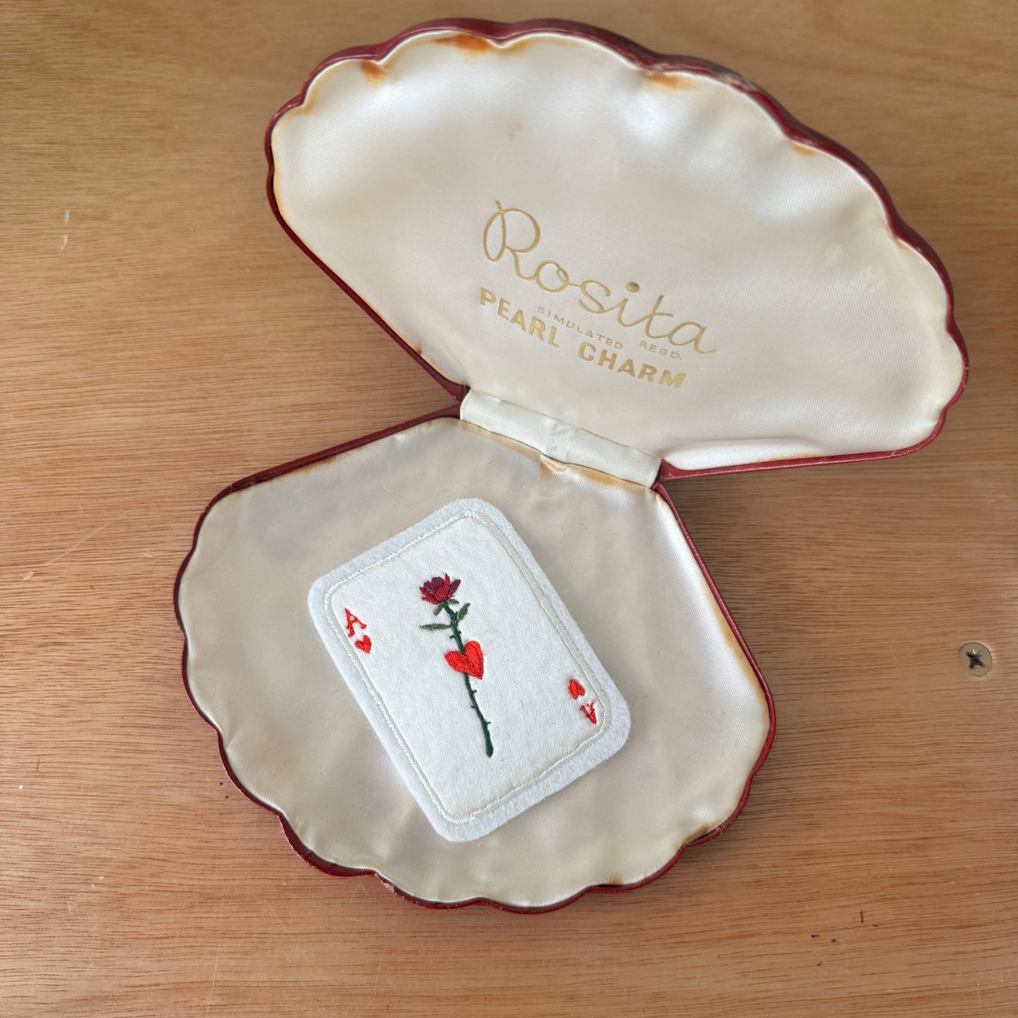 Open shell-shaped jewelry box with 'Rosita Pearl Charm' branding on a wooden surface.