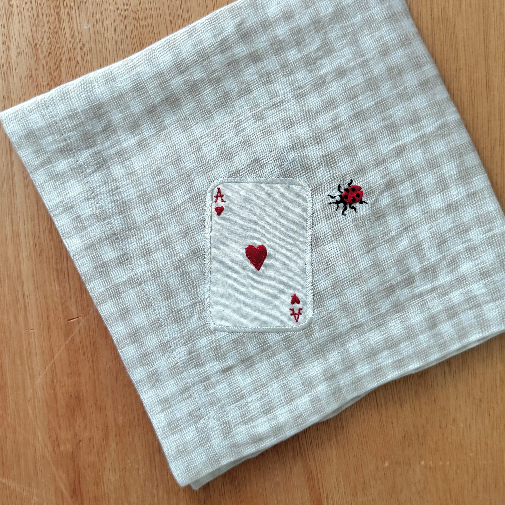 Folded napkin with embroidered card and heart design on a wooden surface