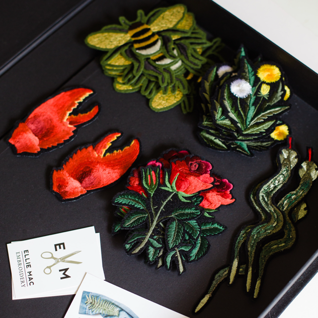 A collection of Ellie Mac Embroidery patches including red rose, dandelion and gold foil bee in a black box