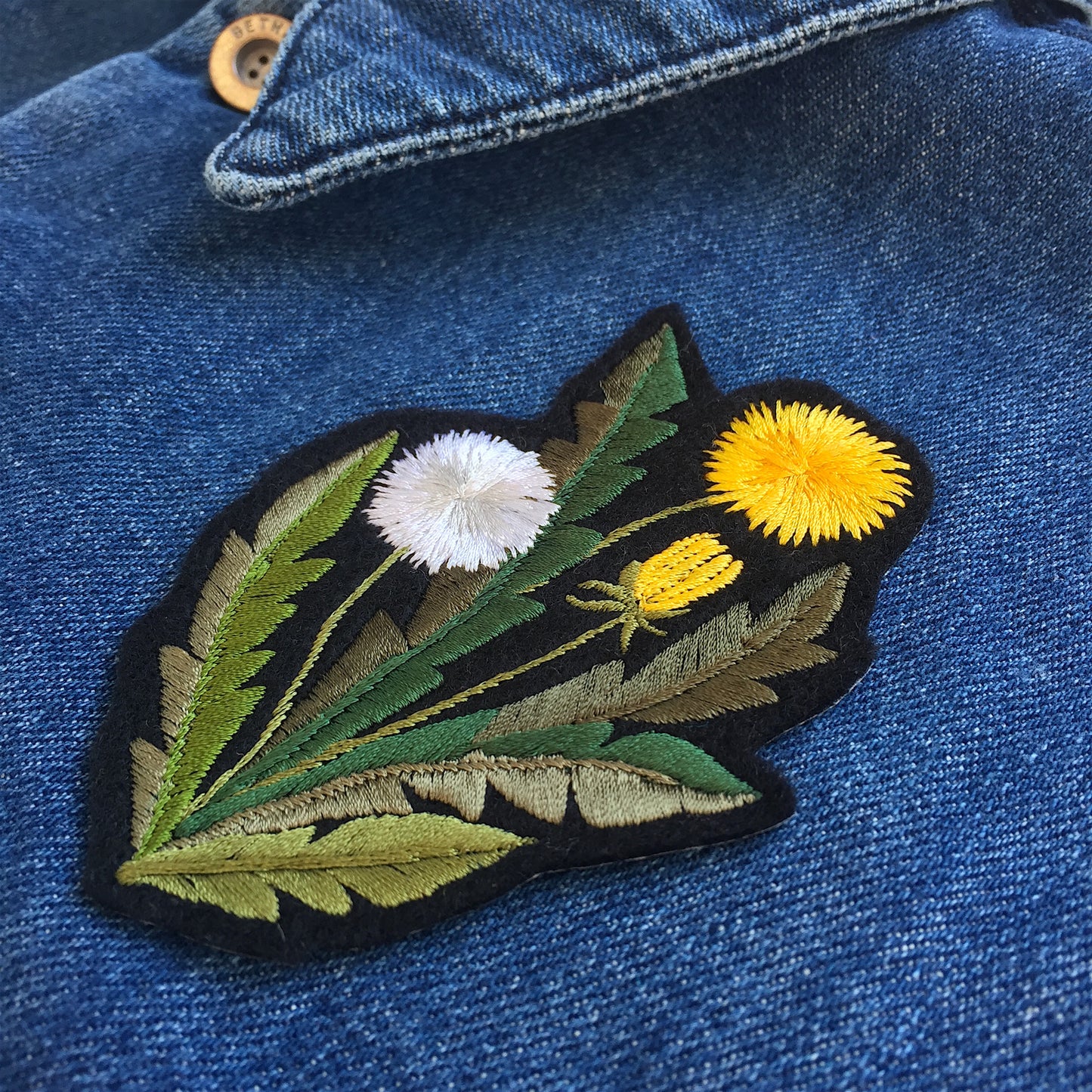 Dandelion embroidered patch shown on front on denim overshirt