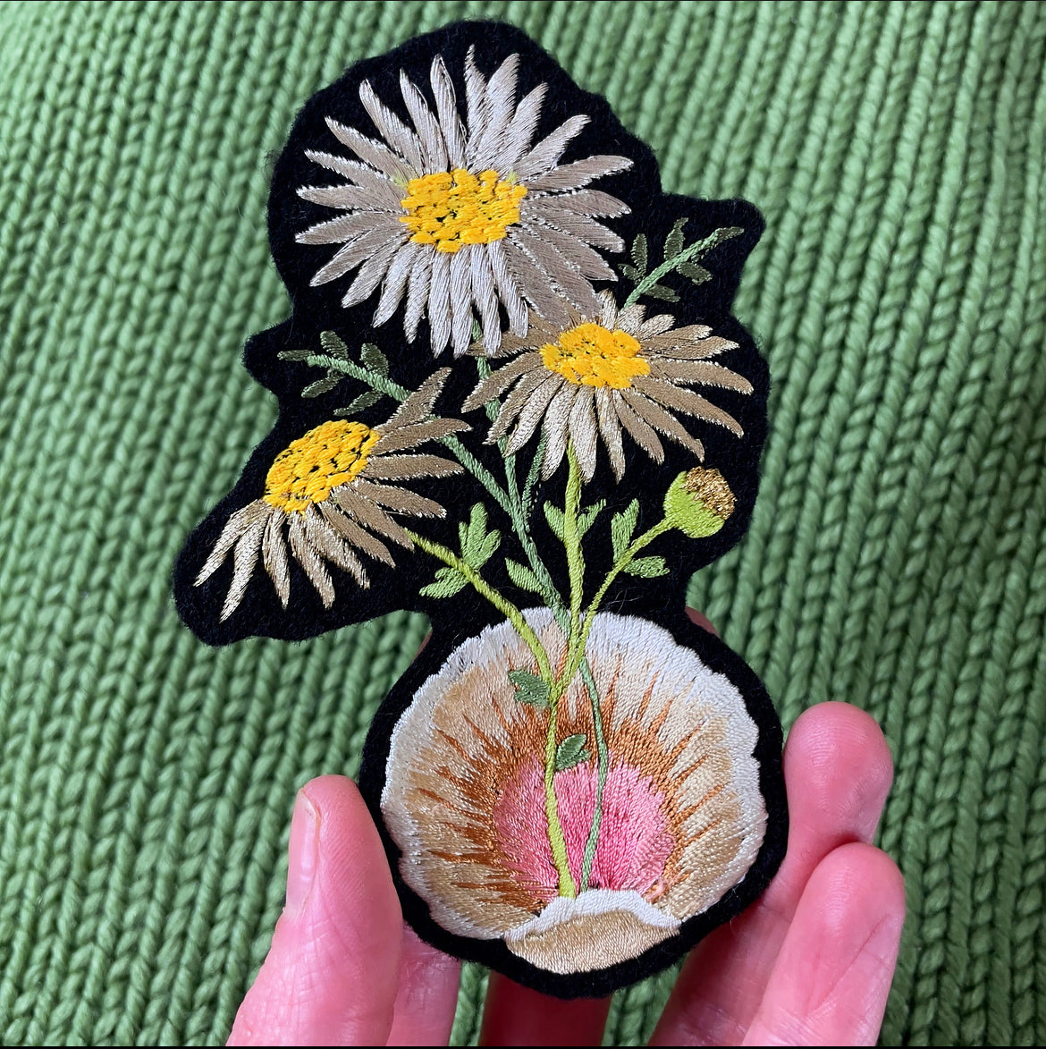 Metallic Daisy & Shell Embroidered Patch held in a hand over a green background
