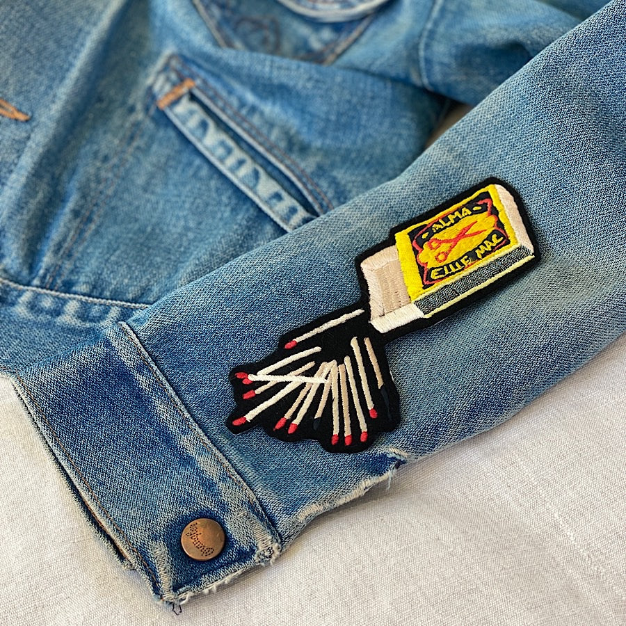 Embroidered matchbox shown on sleeve of denim jacket