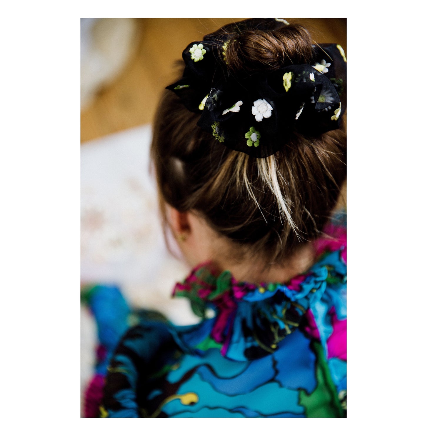 The back of a seated person is seen with the silk organza embroidered scunchie on the bun of their brunette hair