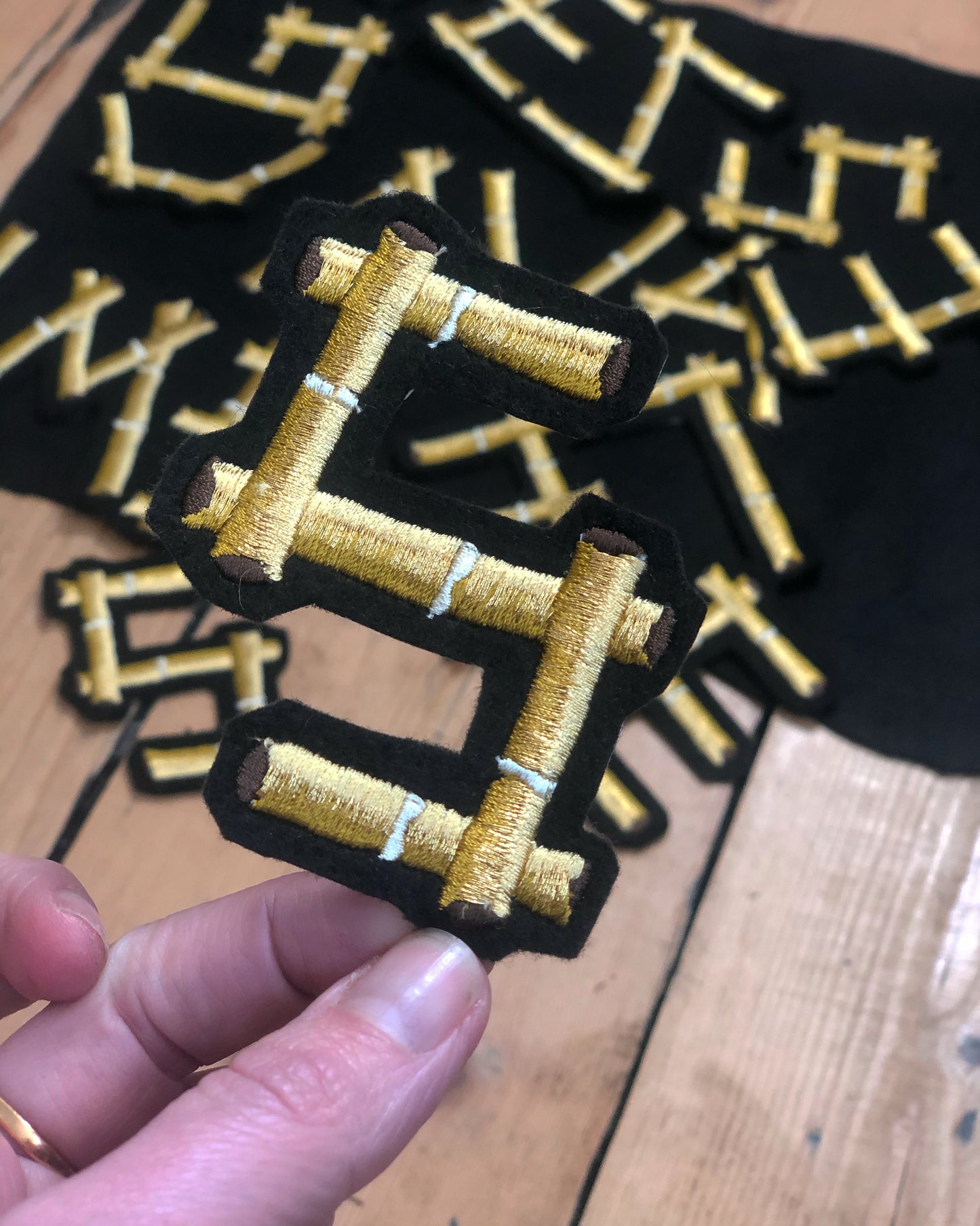 Bamboo embroidered letter S held by a hand with other letters seen in the background