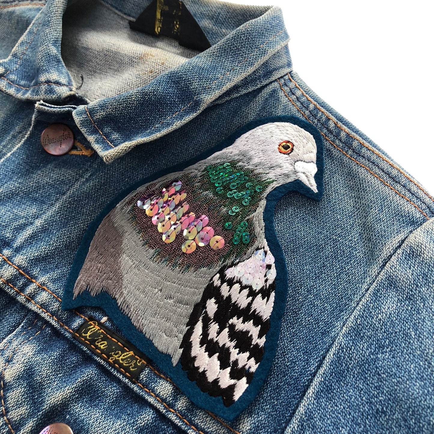 Sparkly pigeon portrait seen on the front shoulder of a blue denim jacket