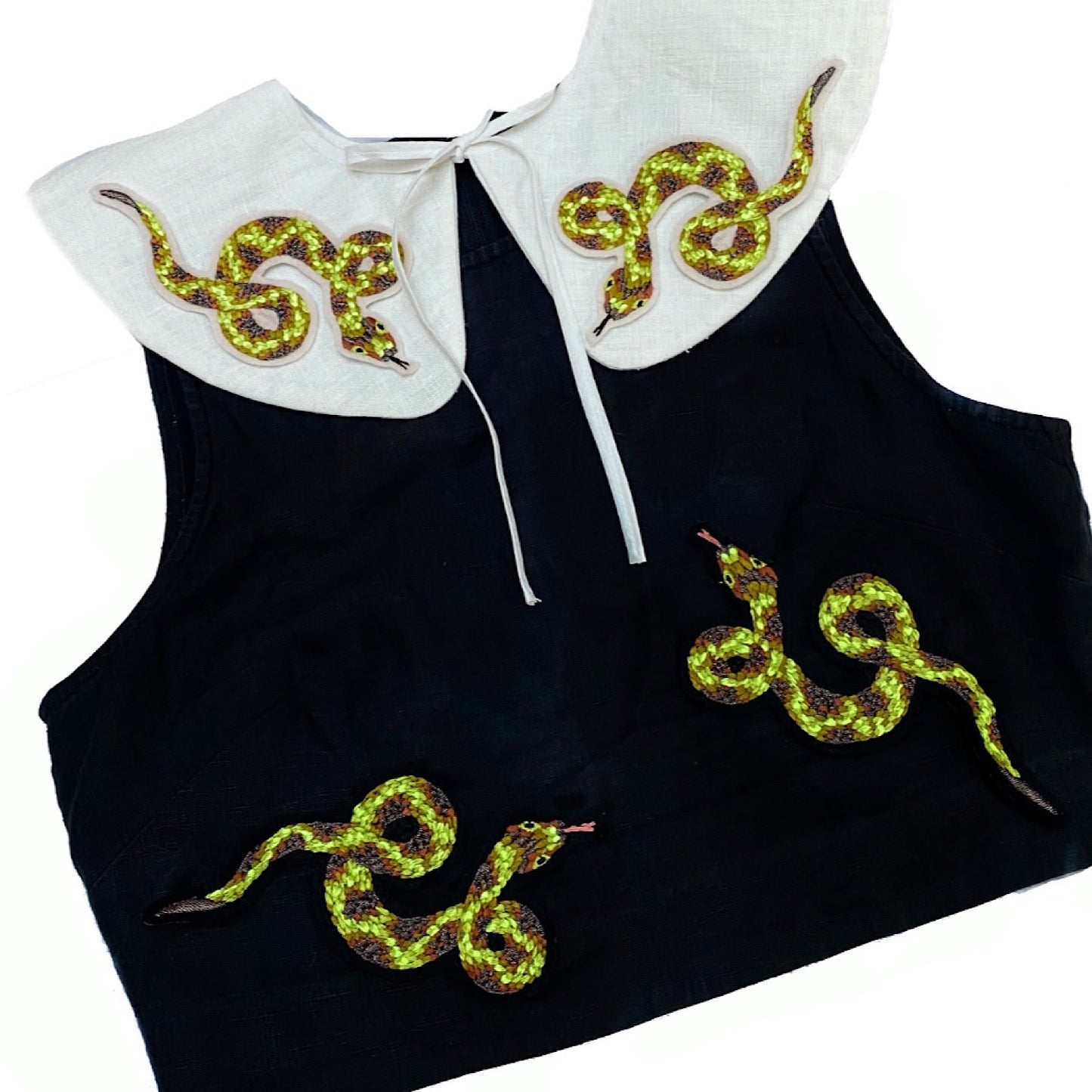 Black sleeveless top with large white collar with four snake embroidered patches placed on the collar and the body of the top 