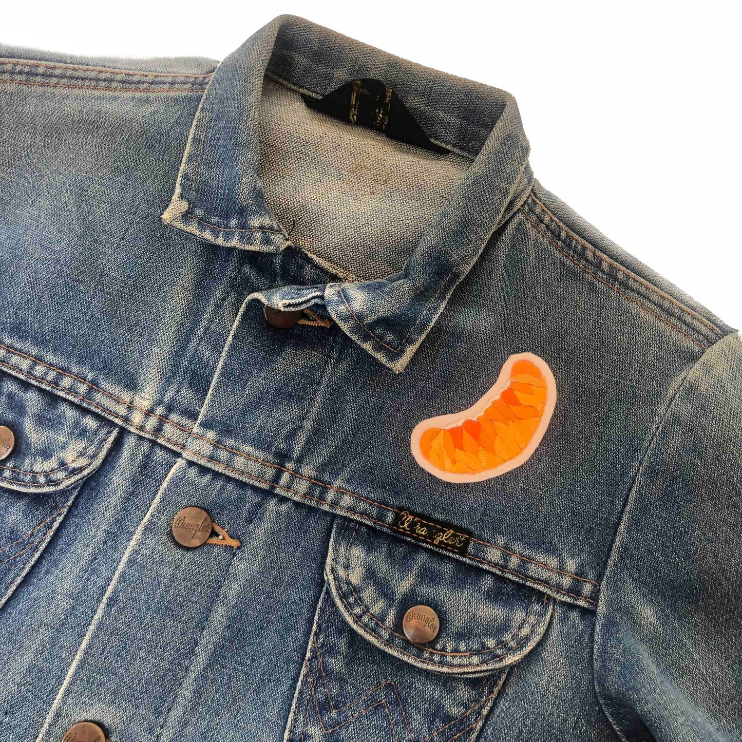 Orange slice embroidered patch on front shoulder of a blue denim jacket