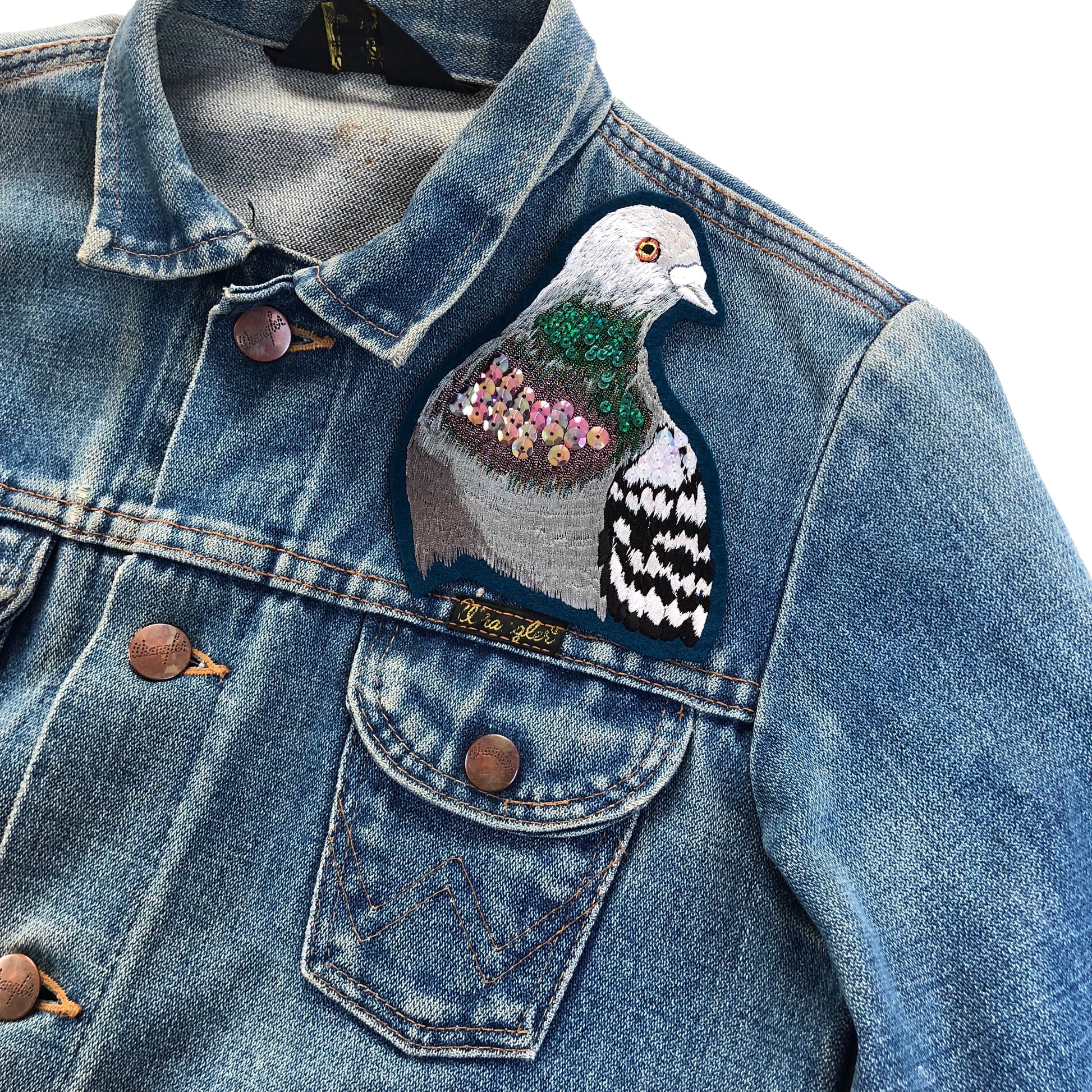Sparkly pigeon portrait seen on the front shoulder of a blue denim jacket