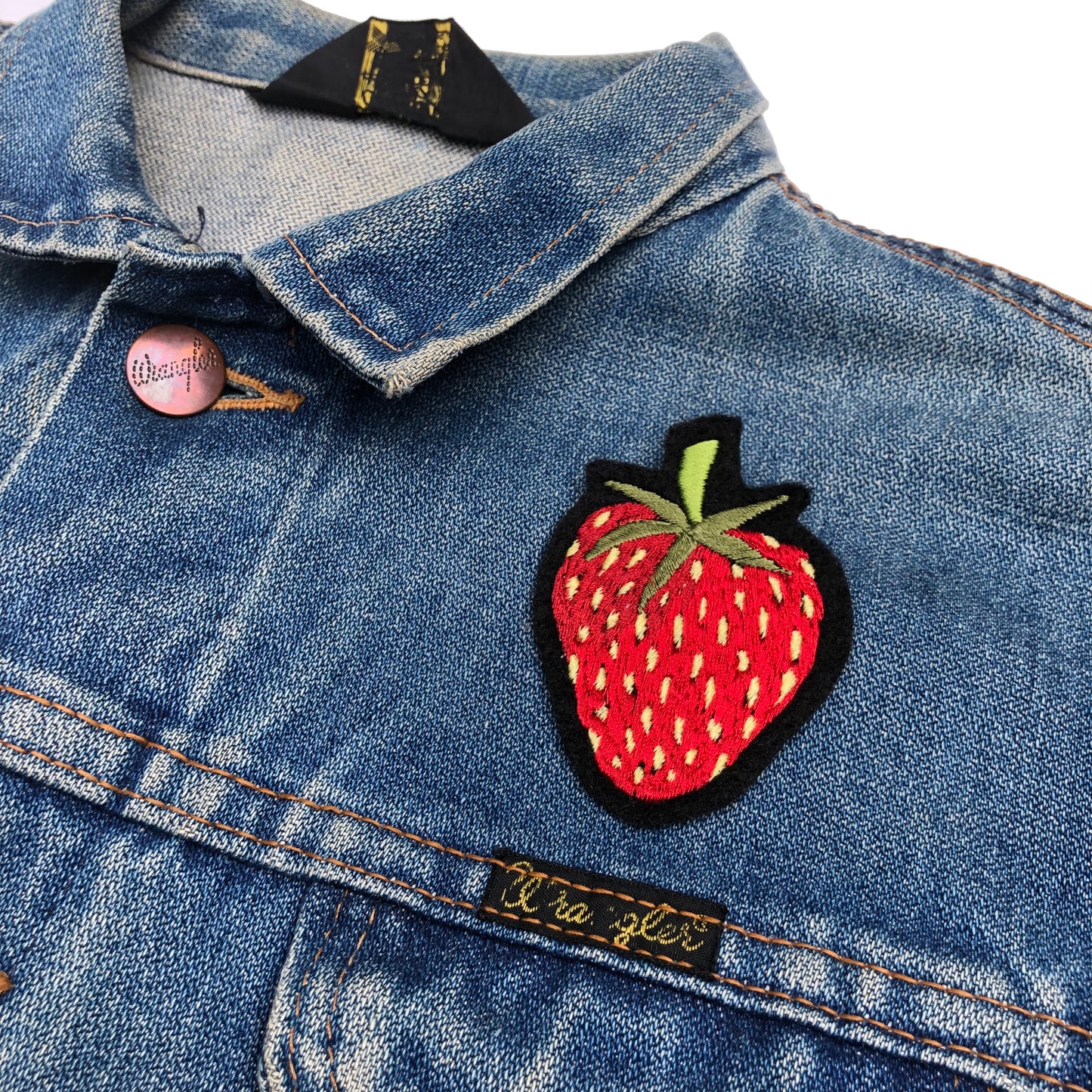 Close-up of strawberry embroidered patch on front shoulder of blue denim jacket