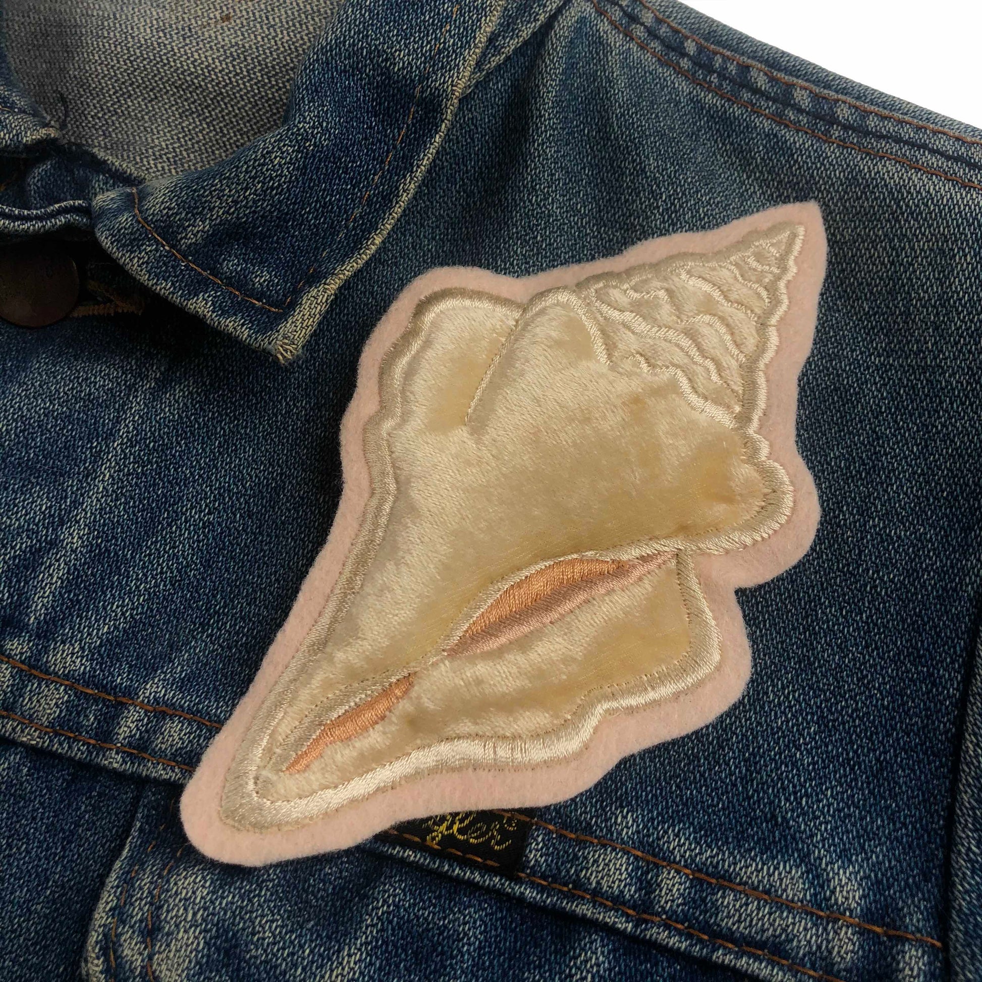 Close-up of velvet conch shell embroidered patch on blue denim jacket