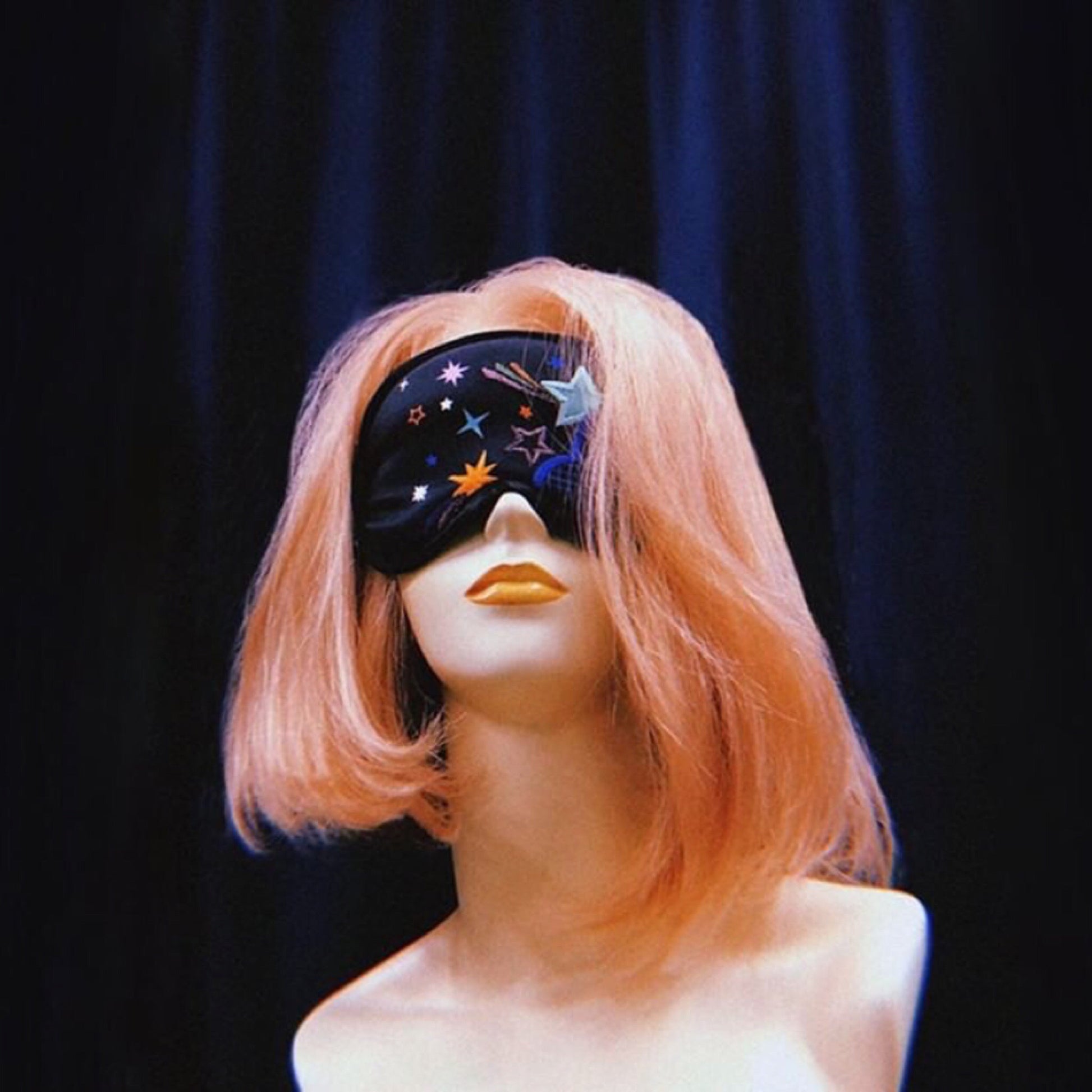Disco nap eye mask on a plastic mannequin head with shoulders just visible. The mannequin has pink hair and is seen in front of a dark navy curtain