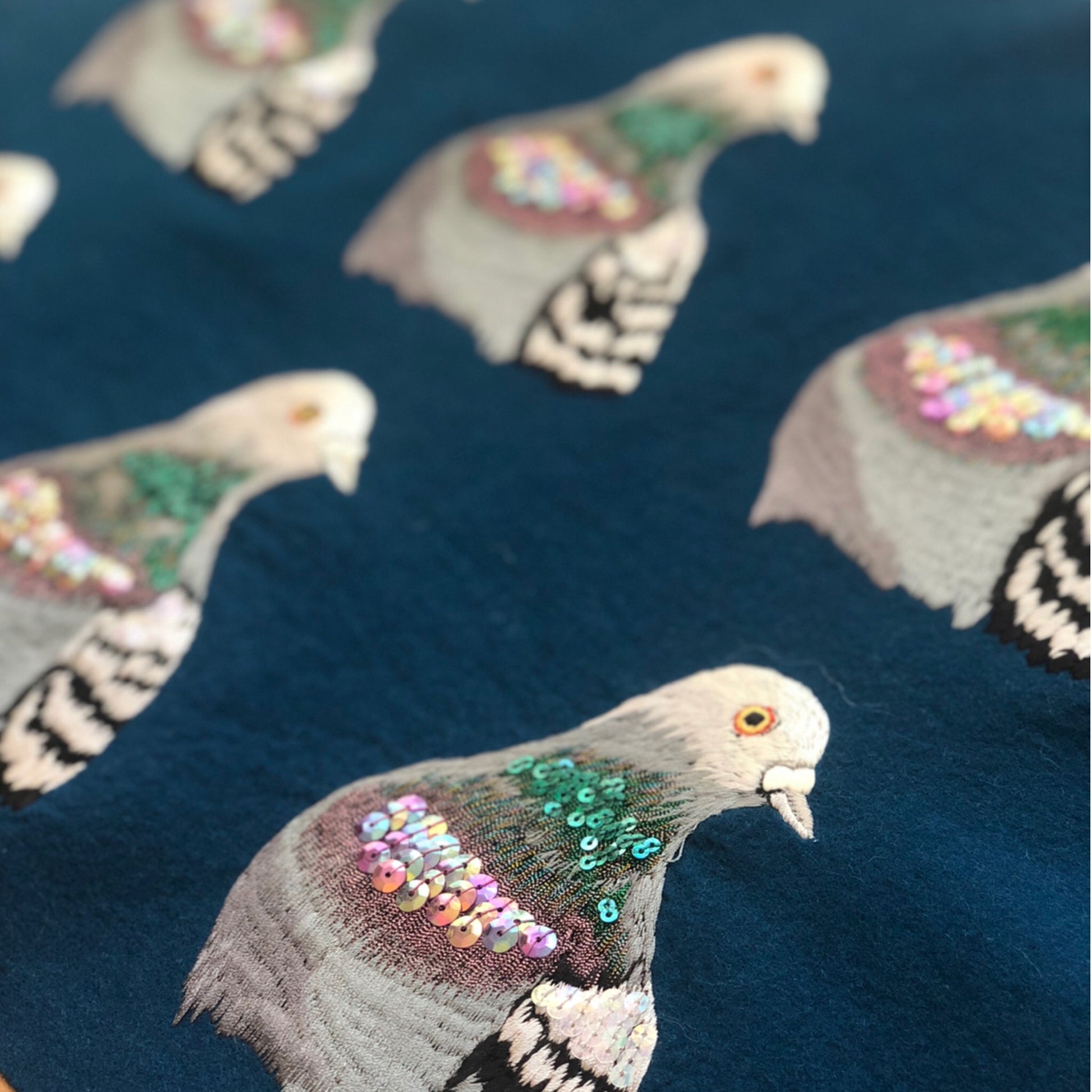 A number of pre-cut sparkly pigeon portrait's on navy felt background. The pigeons in the background are slightly out of focus with the focus being on the one in the bottom right corner