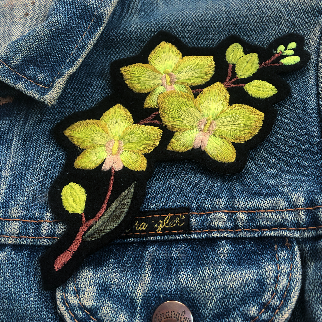 Close-up of orchid embroidered patch on front shoulder of blue denim jacket