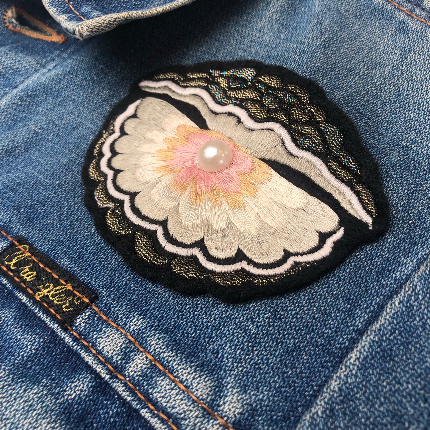 Close-up of oyster with pearl embroidered patch on a denim jacket