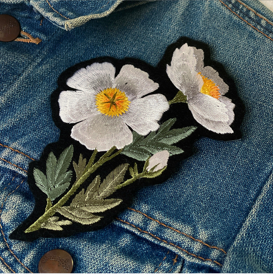 Close-up of a fried egg flower embroidered patch on a blue denim jacket