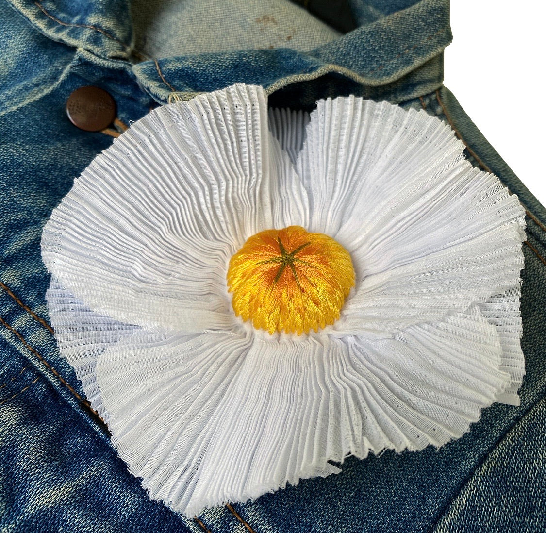 Close-up of pleated fried egg flower embroidery on a blue denim jacket